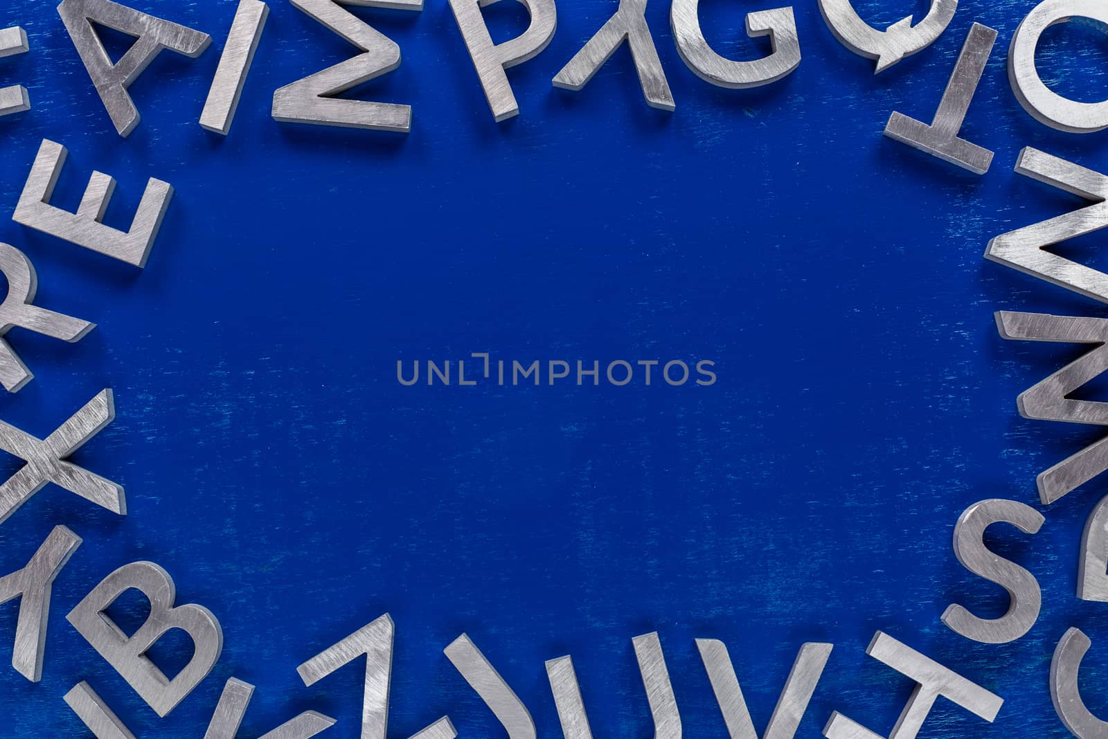 Frame mockup made of of silver metal english alphabet characters on blue background. Usable for back to school or language education projects.