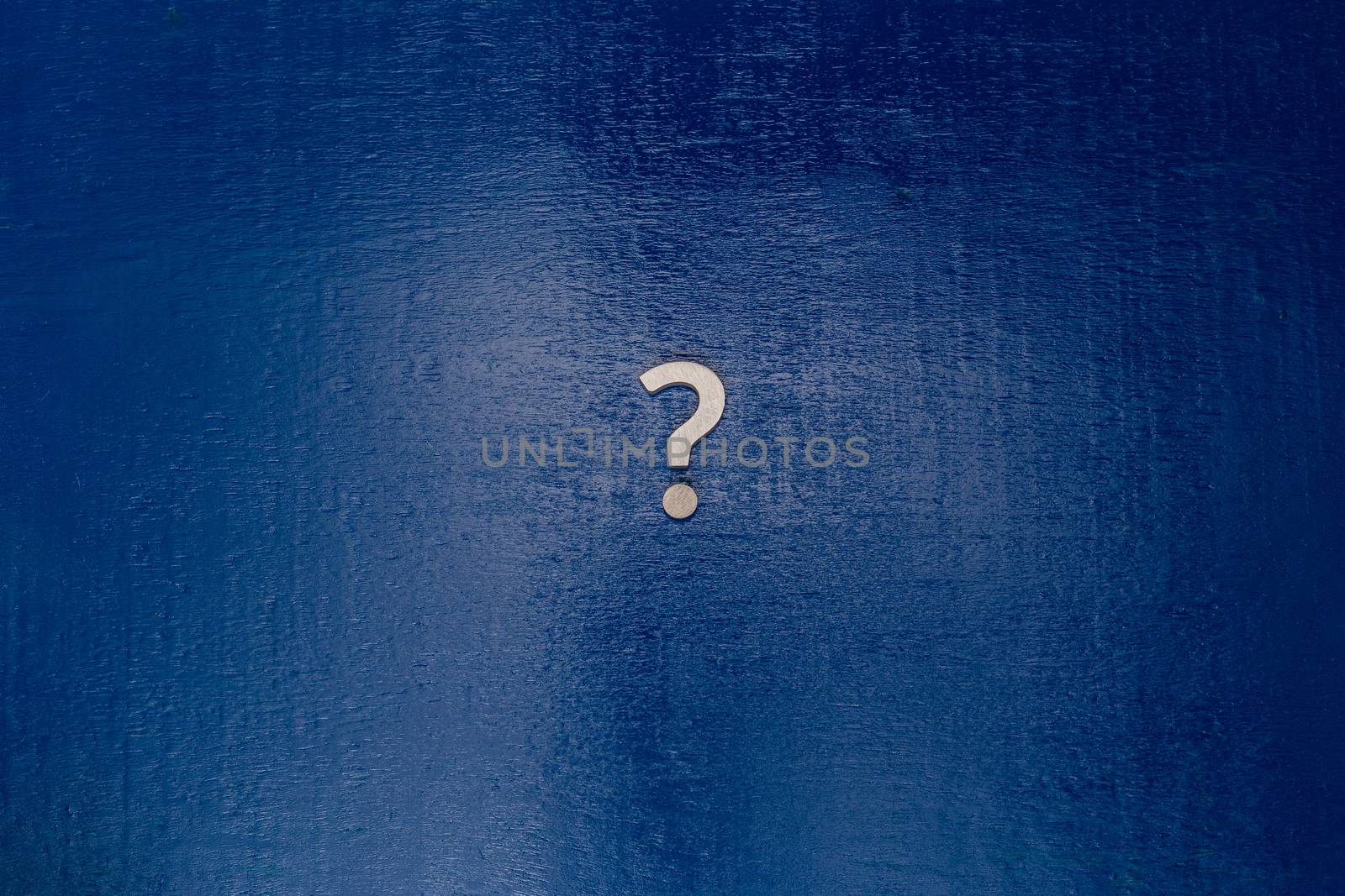 A small white metal question sign on center of dark blue painted board - flat lay conept by z1b