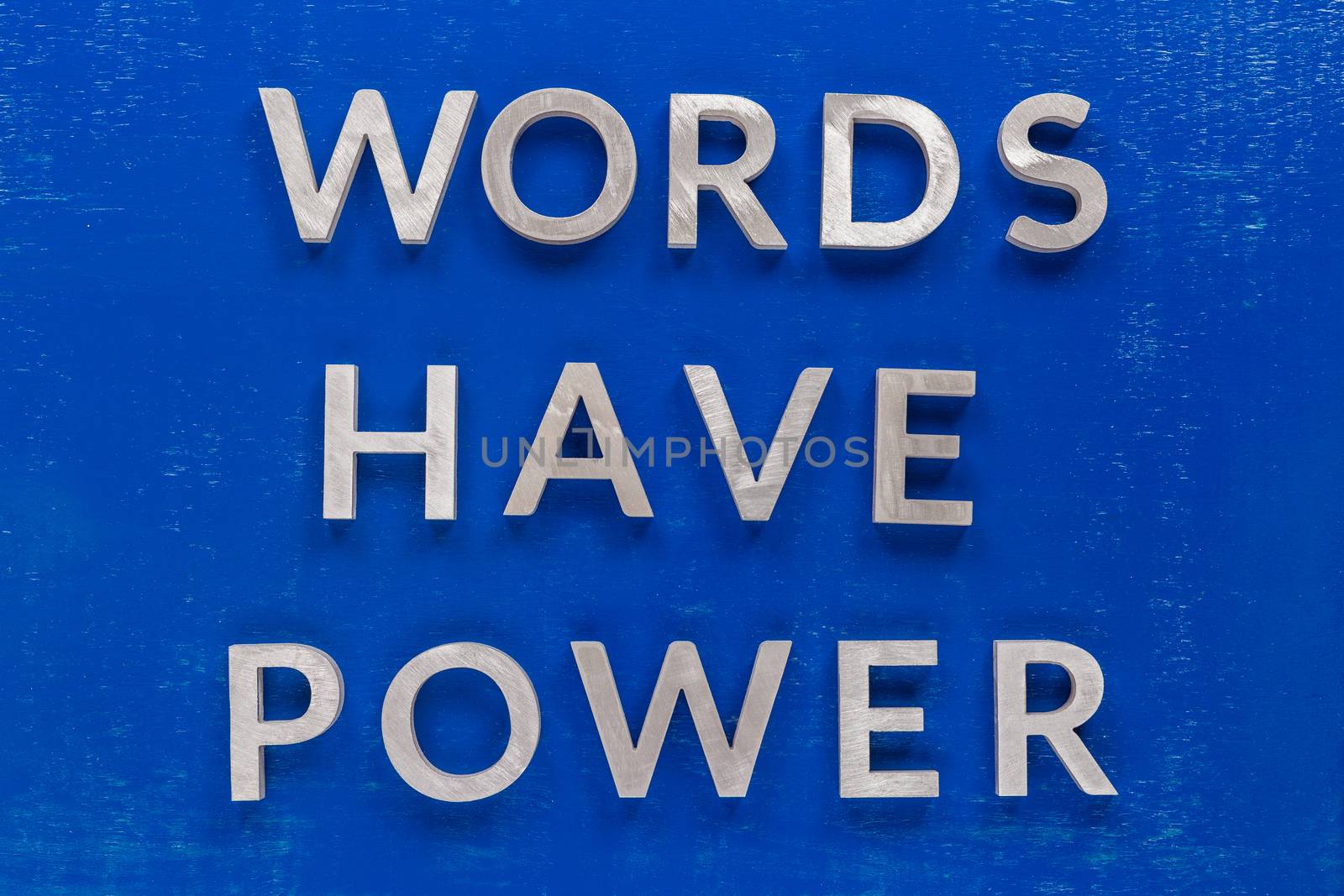 The phrase words have power laid on blue painted board with thick silver metal aphabet characters., centered composition concept
