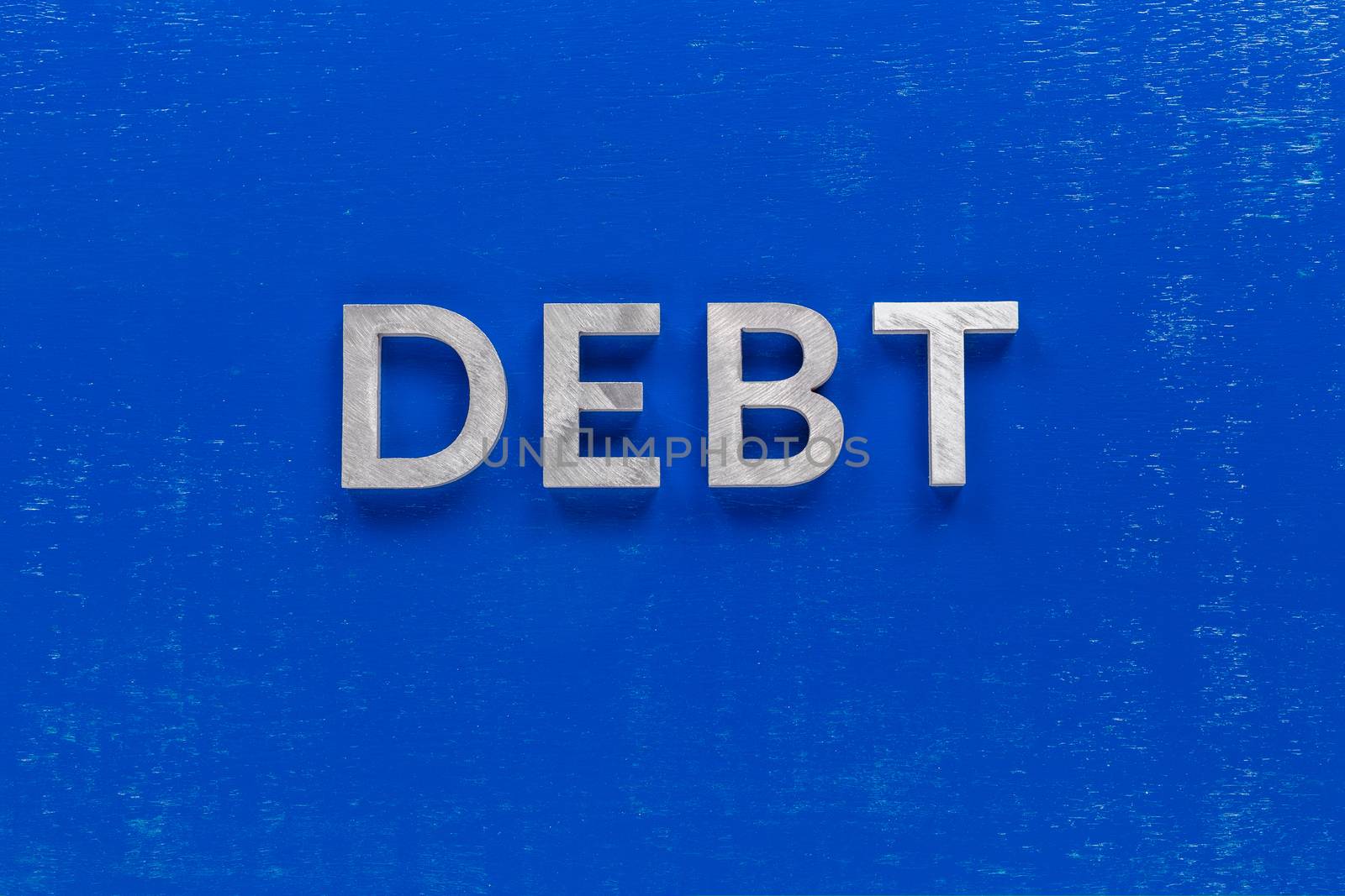 the word debt layed on blue painted board with thick silver metal aphabet characters, centered composition