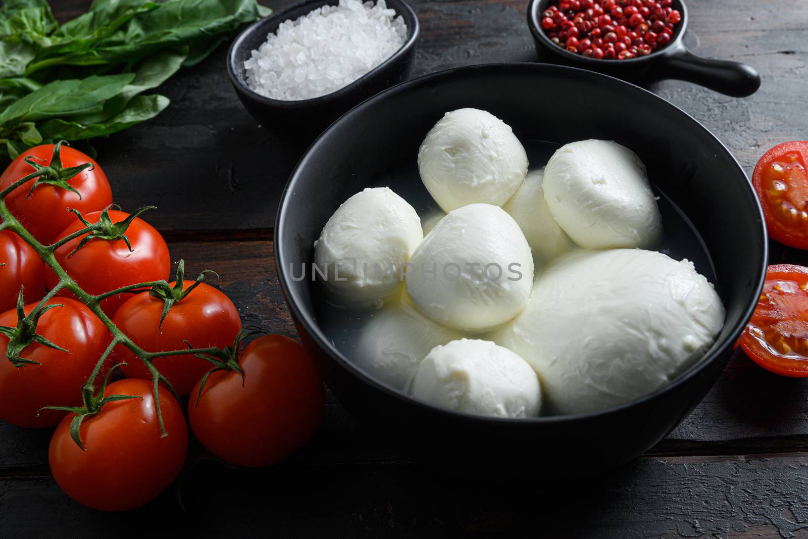 Mozzarella cheese balls, cherry tomatoes and green fresh organic basil peppercorns on wood table selective focus by Ilianesolenyi