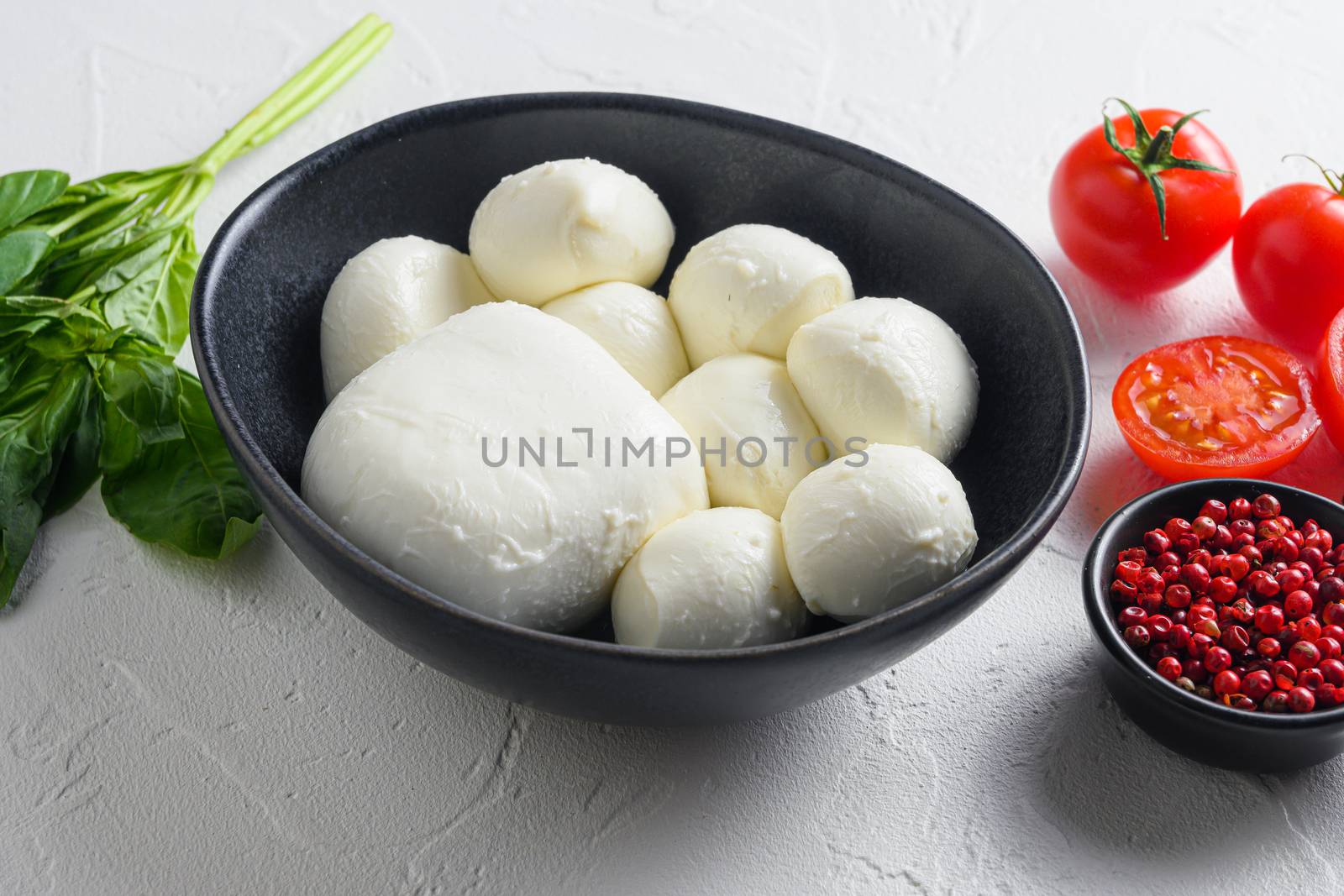 Raw ripe Mozzarella cheese balls with fresh basil leaves and cherry tomatoes, the ingredients , on white background .