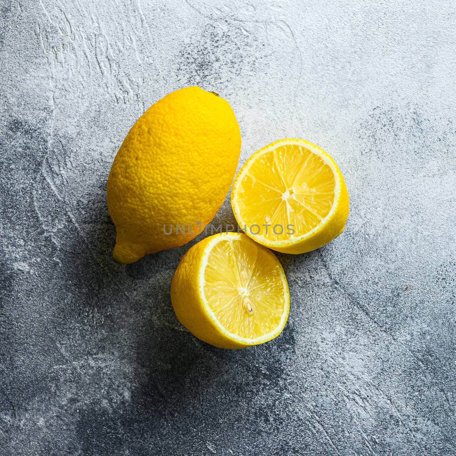 Ripe juicy lemons on gray background. Whole yellow lemon and lemon cut half, top view, vitamin c source by Ilianesolenyi
