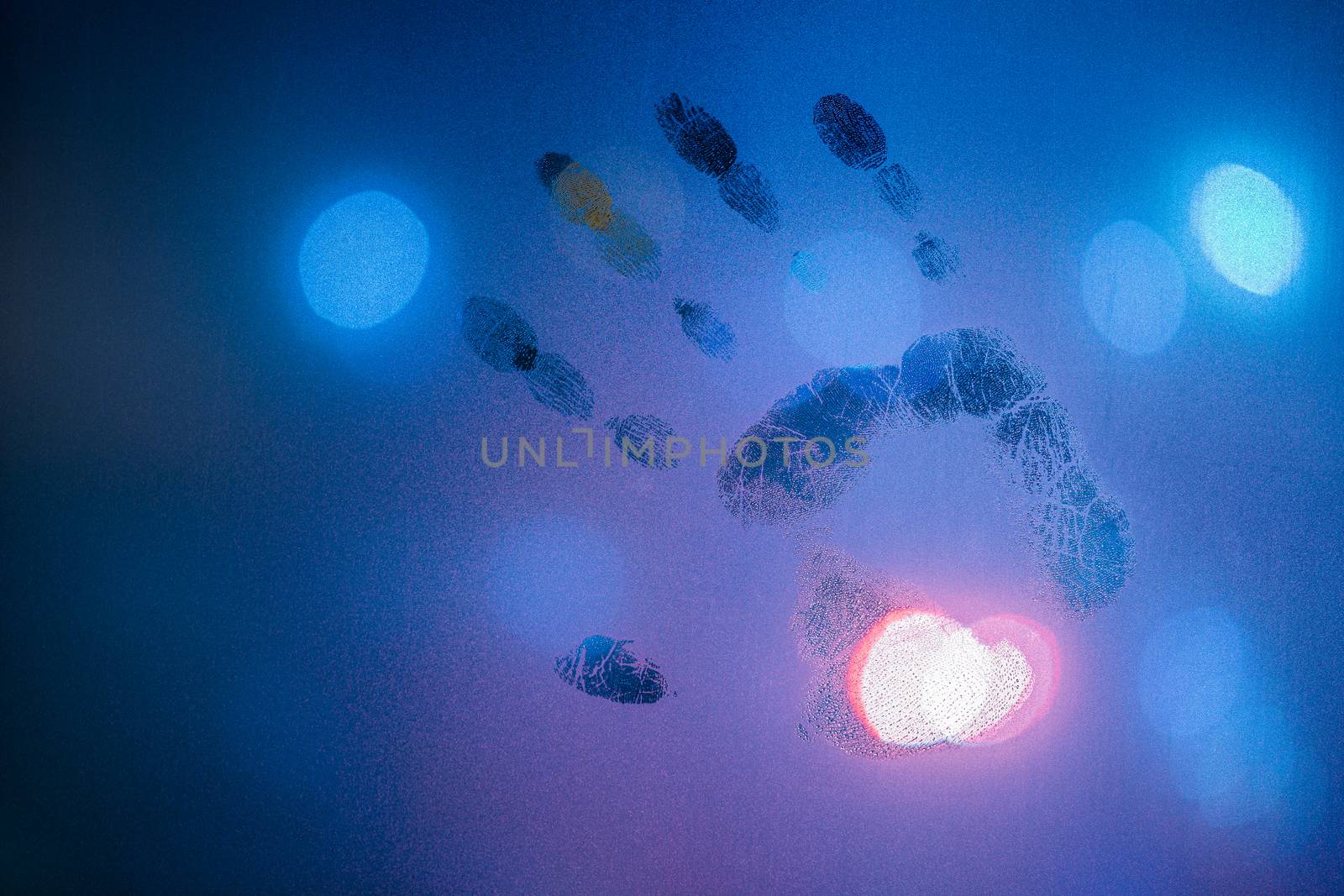 handprint on night wet glass in cold blue colors with blurry street light in backround.
