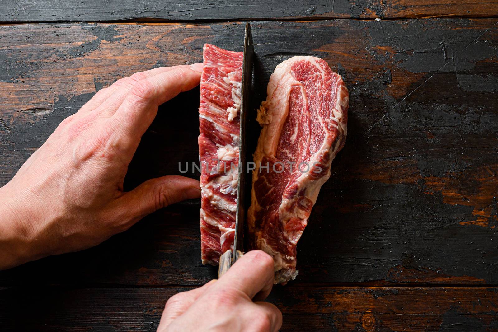 Chuck eye roll steak with butcher hands man cut meat with meat cleaver. Organic beef. at work chop. over dark wooden plank background Space for text.