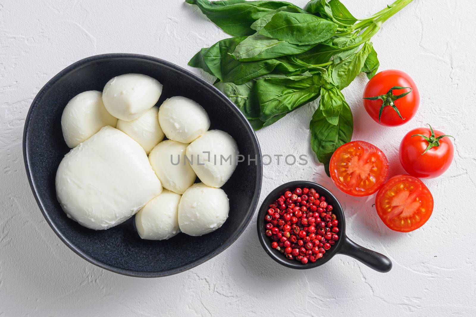Mozzarella cheese balls with fresh basil leaves and cherry tomatoes, the ingredients of the Italian Caprese salad, on white background overhead photo.