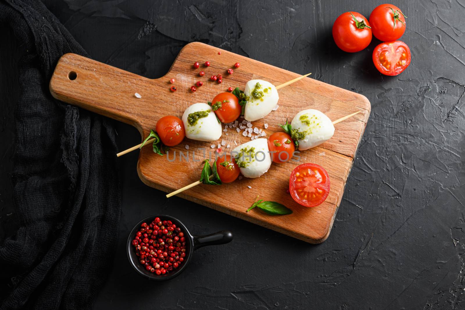 caprese salad skewer with tomato on sticks Italian traditional caprese salad ingredients. Mediterranean food. over black stone background overhead space for text.