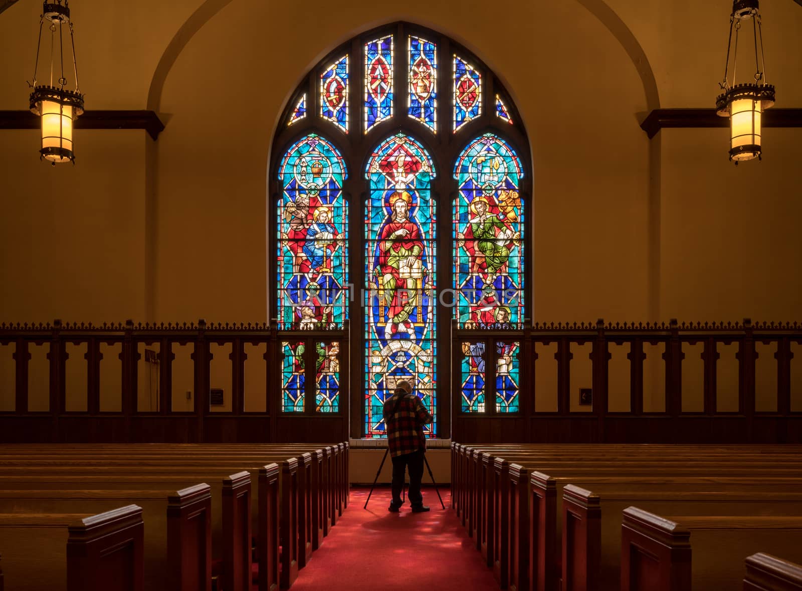 Photographer takes photo from the aisle between pews illuminated by light from stained glass window