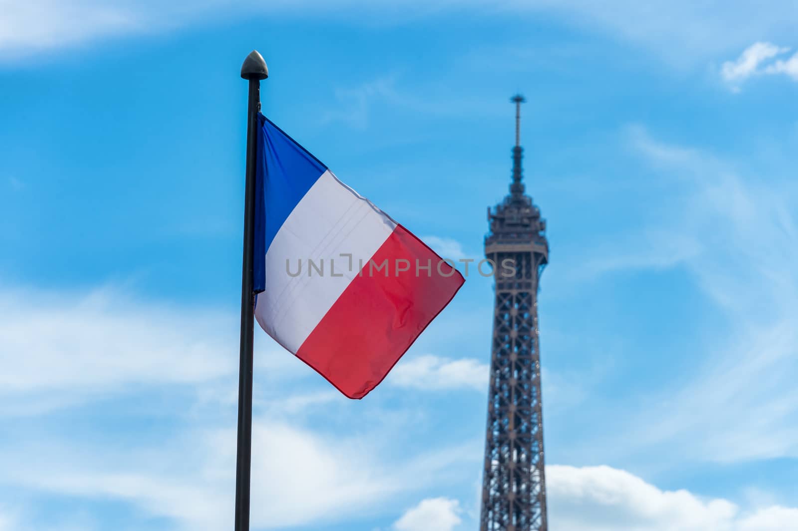 French flag waving against blue sky and Eiffel Tower