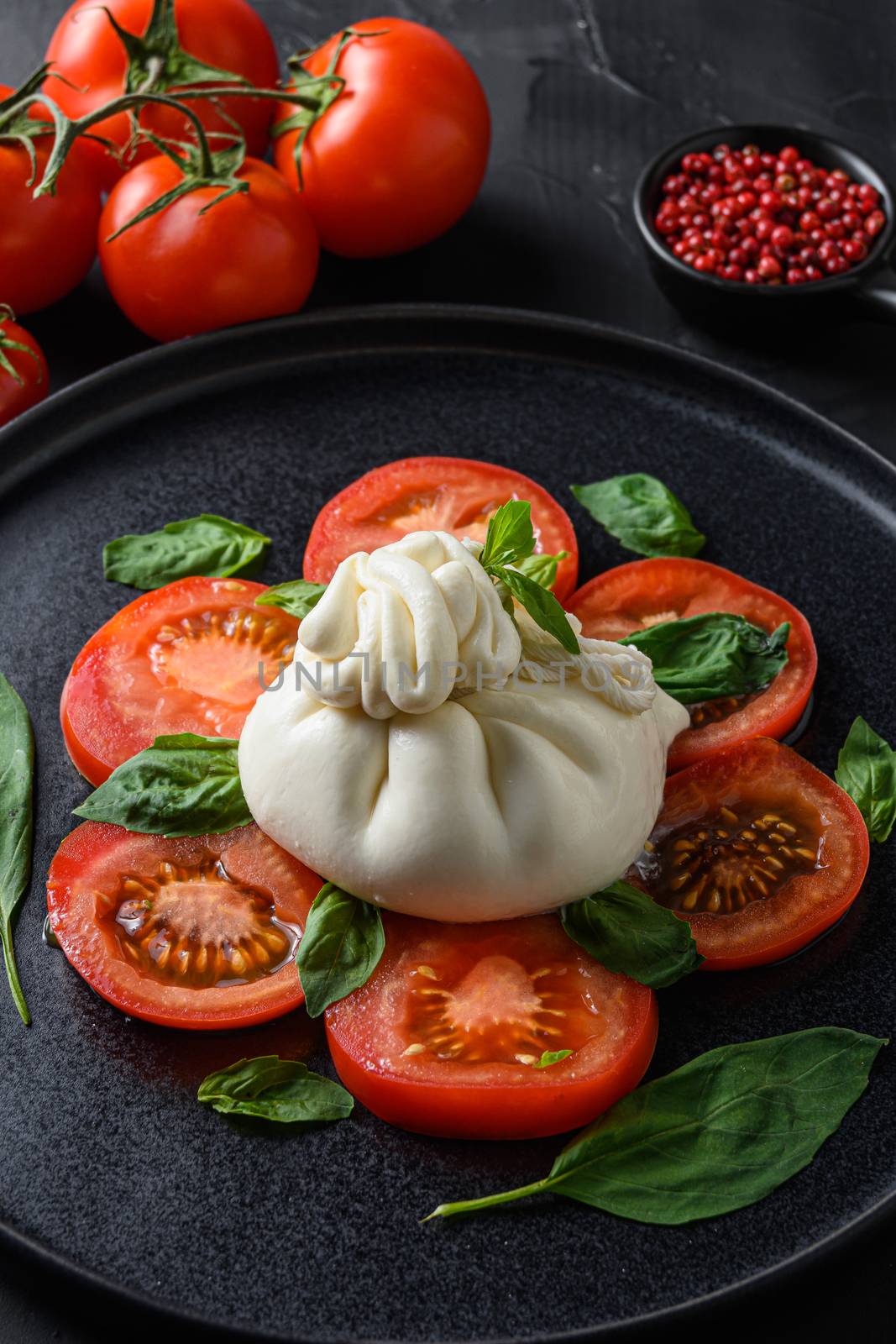 Buffalo burrata cheese served with fresh tomatoes and basil leaves. on a black stone background