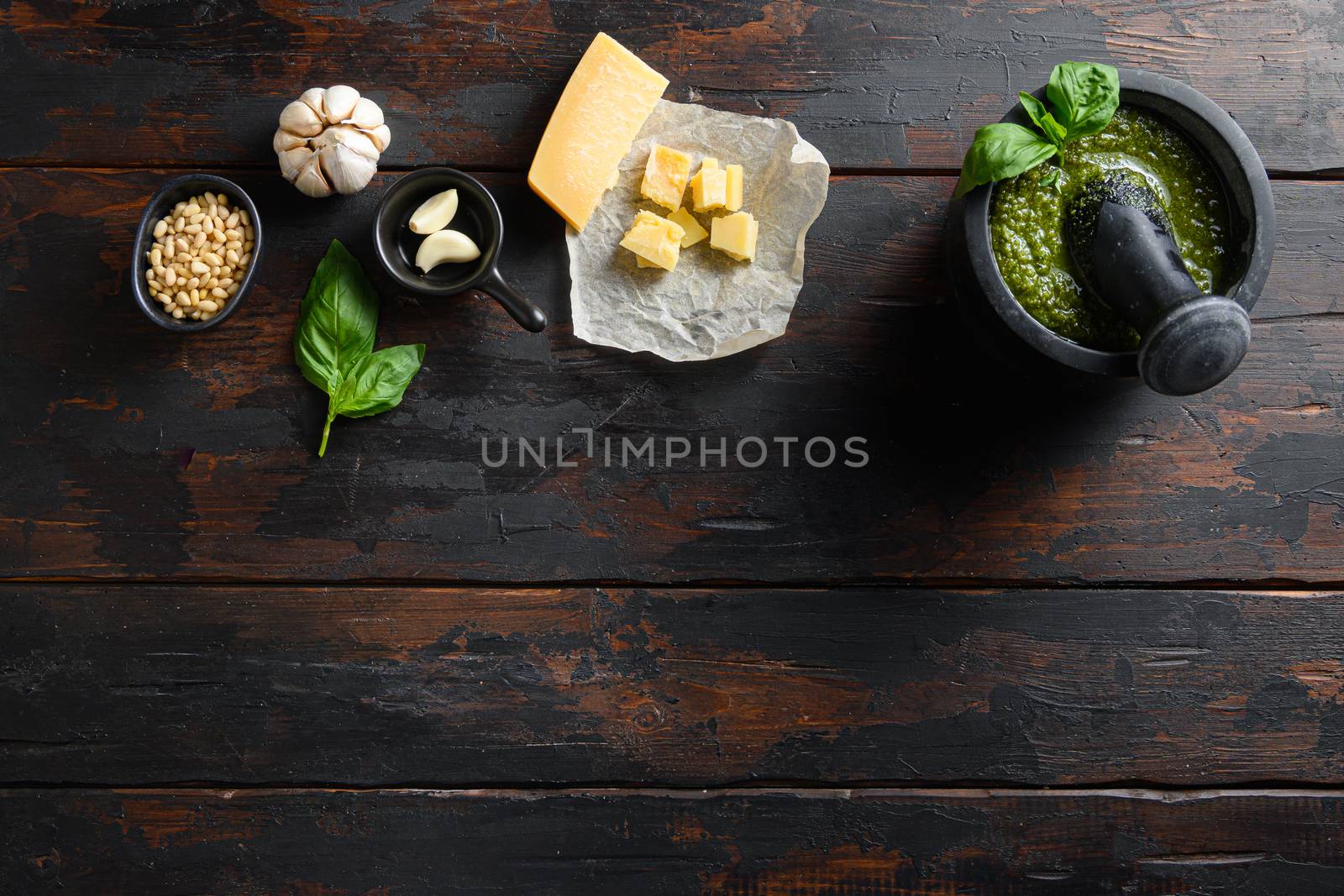 fresh Green basil pesto in mortar preparation in black mortar with italian recipe ingredients over old wood table copy space for text overhead