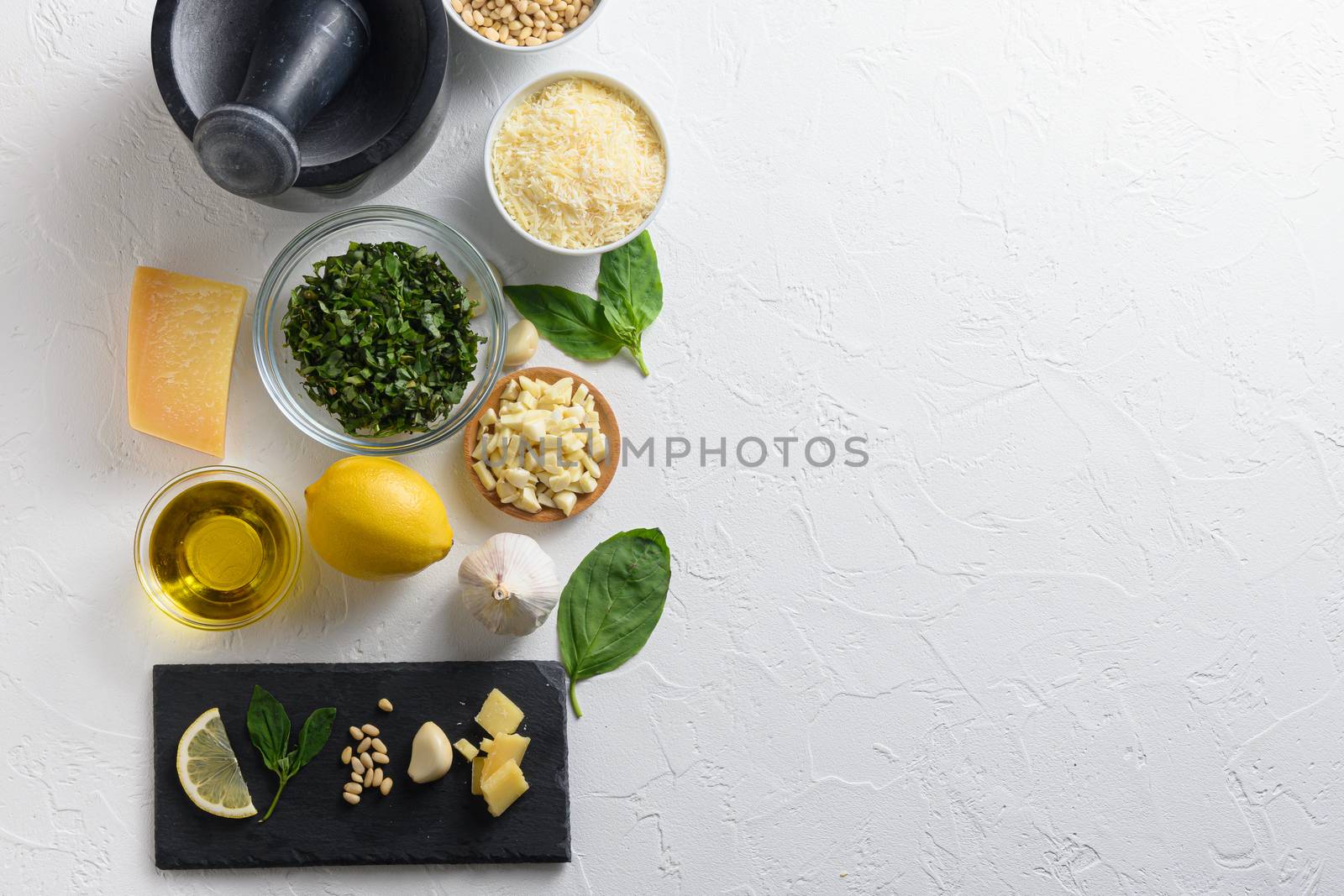 Pesto alla Genovese , Basil Sauce Different ingredients for Italian pesto. Grated parmesan cheese, basil leaves, pine nuts, olive oil, garlic On the white stone slate side top view. space for text on side.