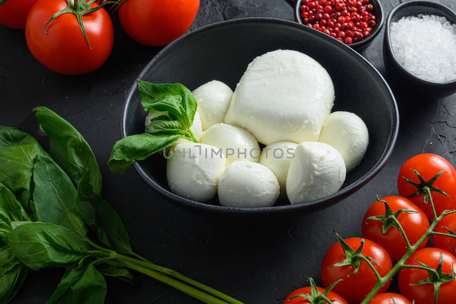 caprese salad ingredients Mozzarella balls, buffalo , tomatoes, basil leaves, olive oil with vinegar pepper salt Italian recipe black stone background. selective focus, copy space. close up by Ilianesolenyi