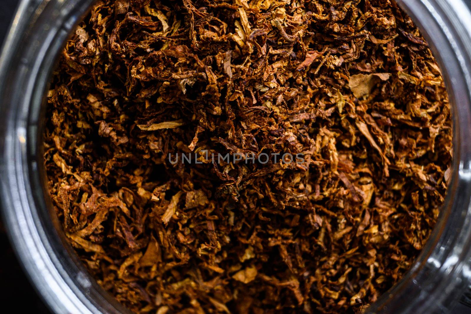 close-up macro Cigar and pile of Cut tobacco leaves of Dried tobacco in glass jars on rustic wood dark table top view overhead