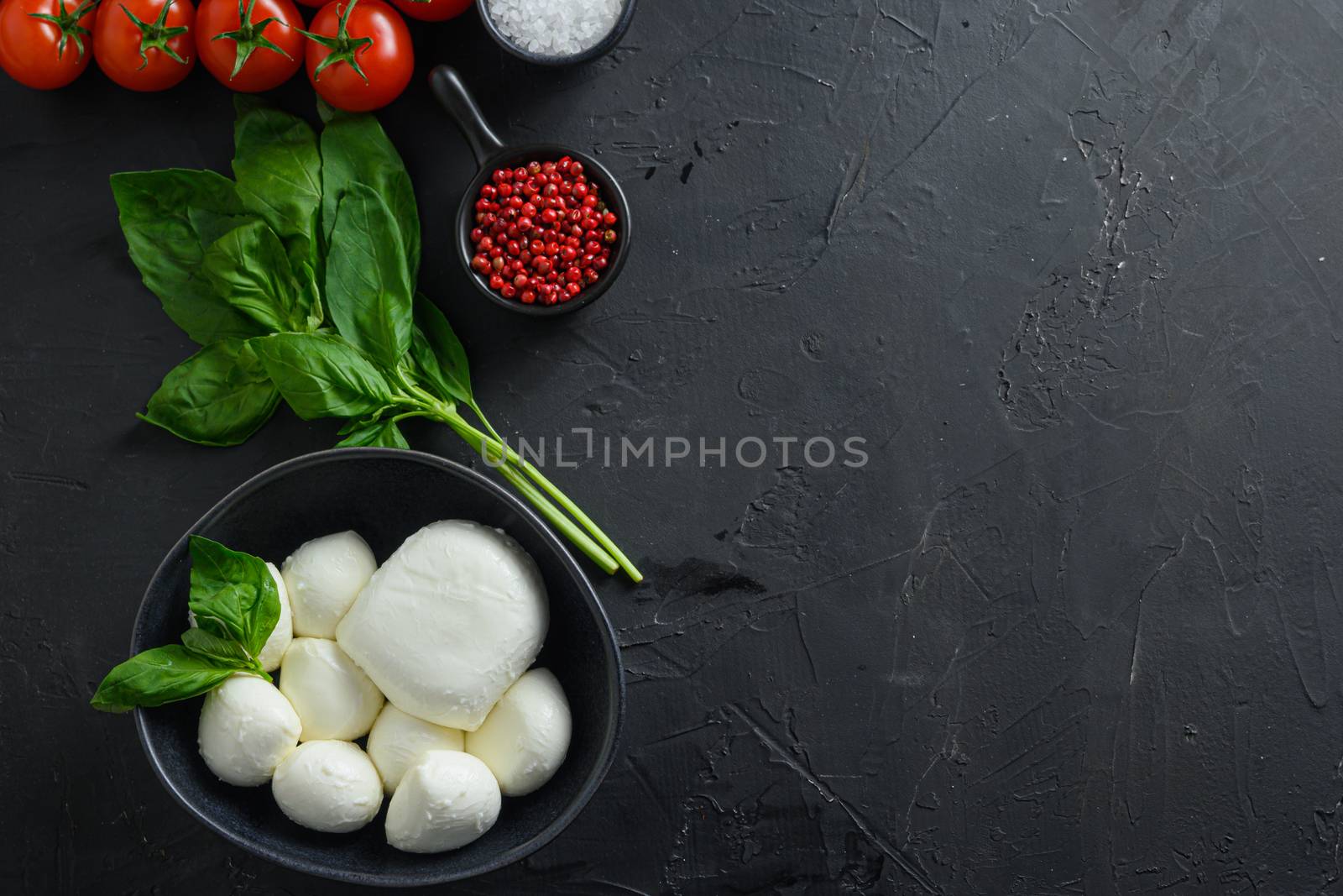 Mini balls of mozzarella cheese,Fresh cherry tomatoes, basil leaf, cheese for caprese salad on black slate stone chalkboard with copyspace. Top view by Ilianesolenyi