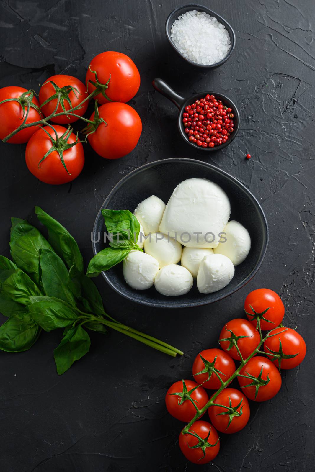 caprese salad ingredients Mozzarella balls, buffalo , tomatoes, basil leaves, olive oil with vinegar pepper salt Italian recipe black stone background. selective focus, copy space. Top view