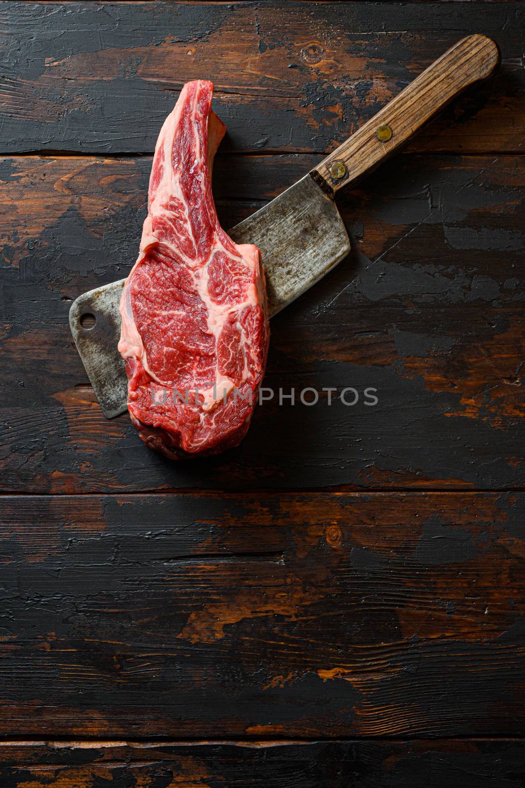 Raw Scotch Fillet steak on meat cleaver. Organic beef. Dark wooden background. Top view. Copy space.