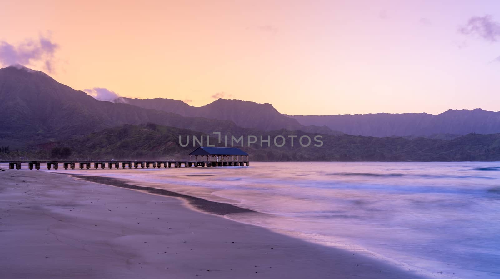 Sunrise lights the dawn sky above Hanalei Pier with the Na Pali coast in the background near Hanalei, Kauai, Hawaii