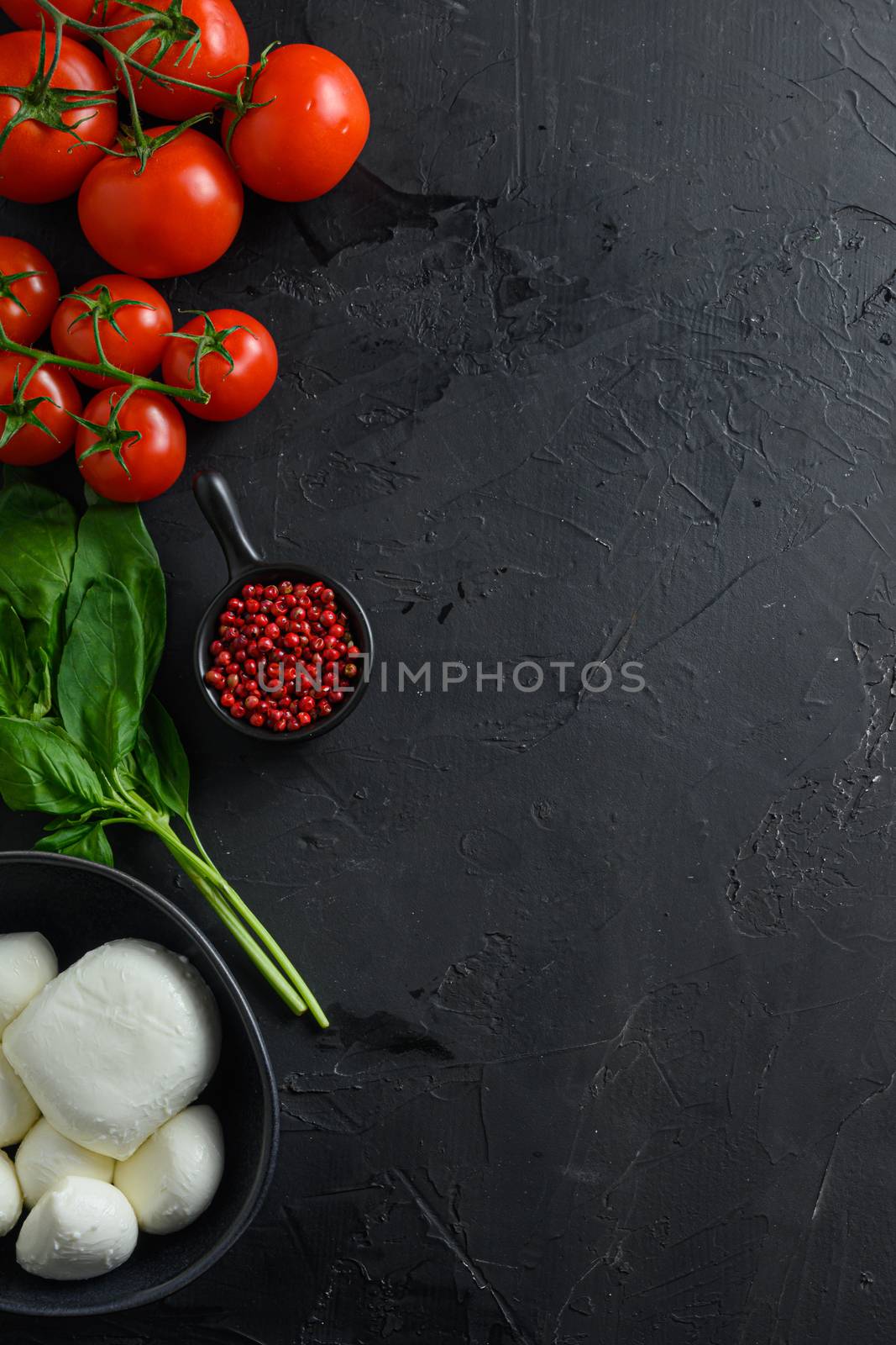 Mini balls of mozzarella cheese,Fresh cherry tomatoes, basil leaf, cheese for caprese salad on black slate stone chalkboard with vertical space for text . Top view