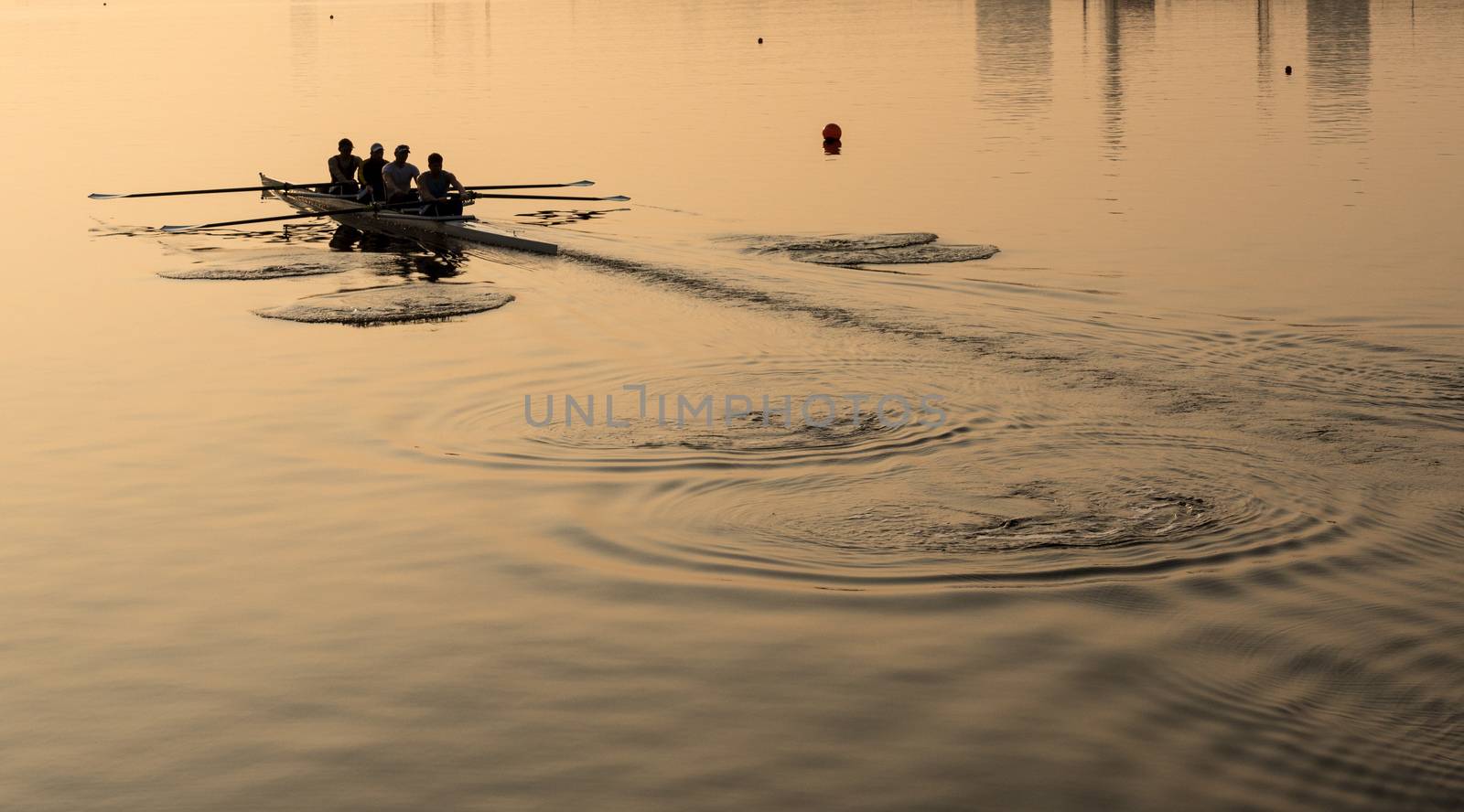 Sunrise lights up team of four rowers in canoe practicing in London Docklands