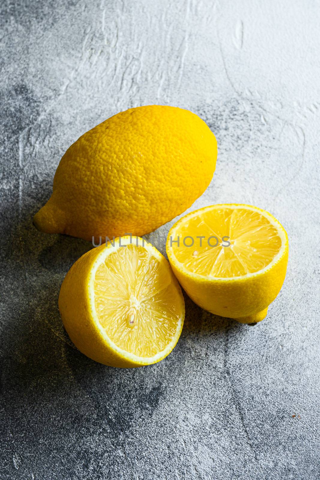 Delicious sliced citrus fruit Whole yellow lemon and lemon cut half, top view, copy space. Fresh citrus fruits, vitamin c source on grey background.