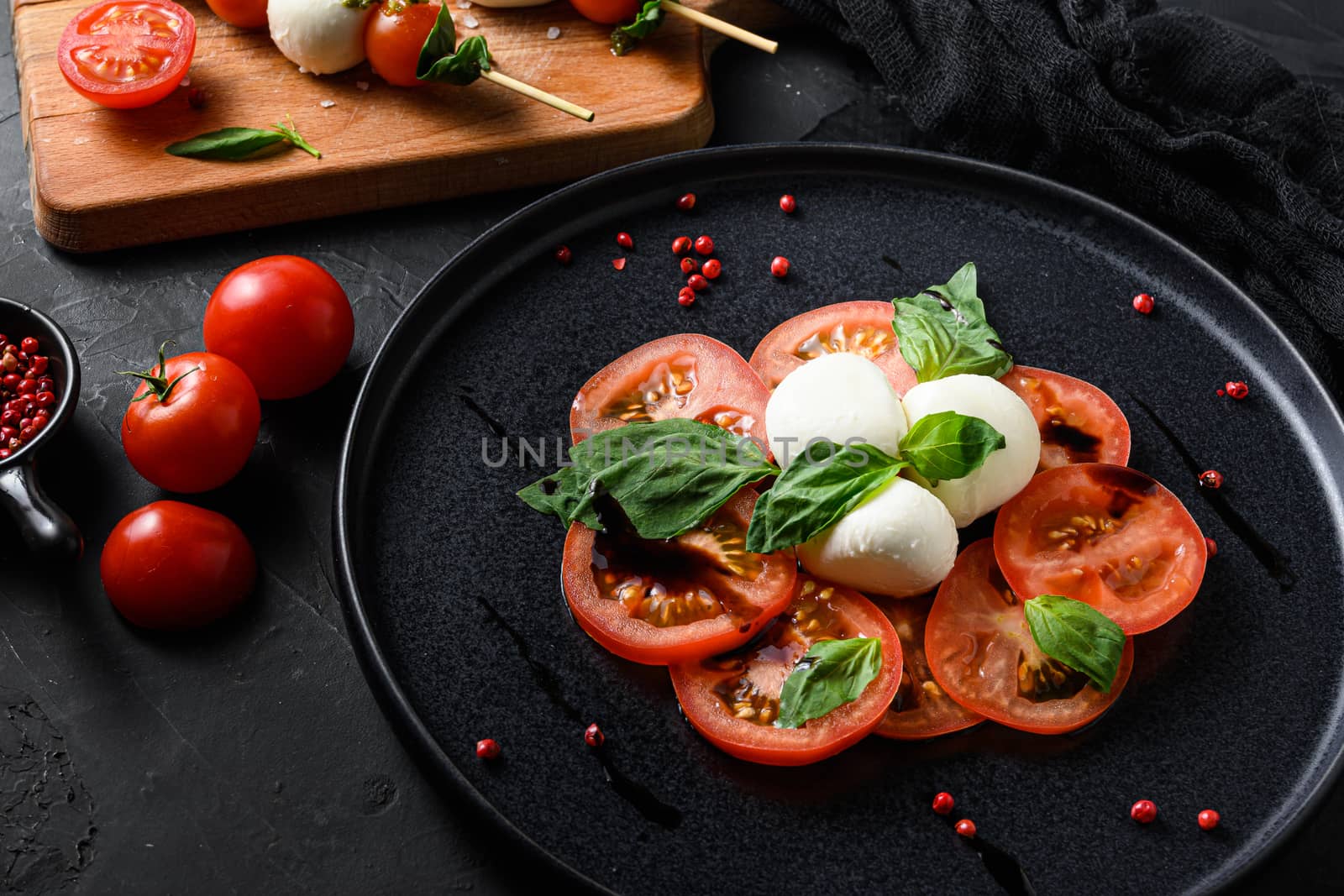 Caprese salad Tomato and mozzarella slices with basil leaves on sticks skewer and on black ceramic platwantipasta black textured background selective focus.