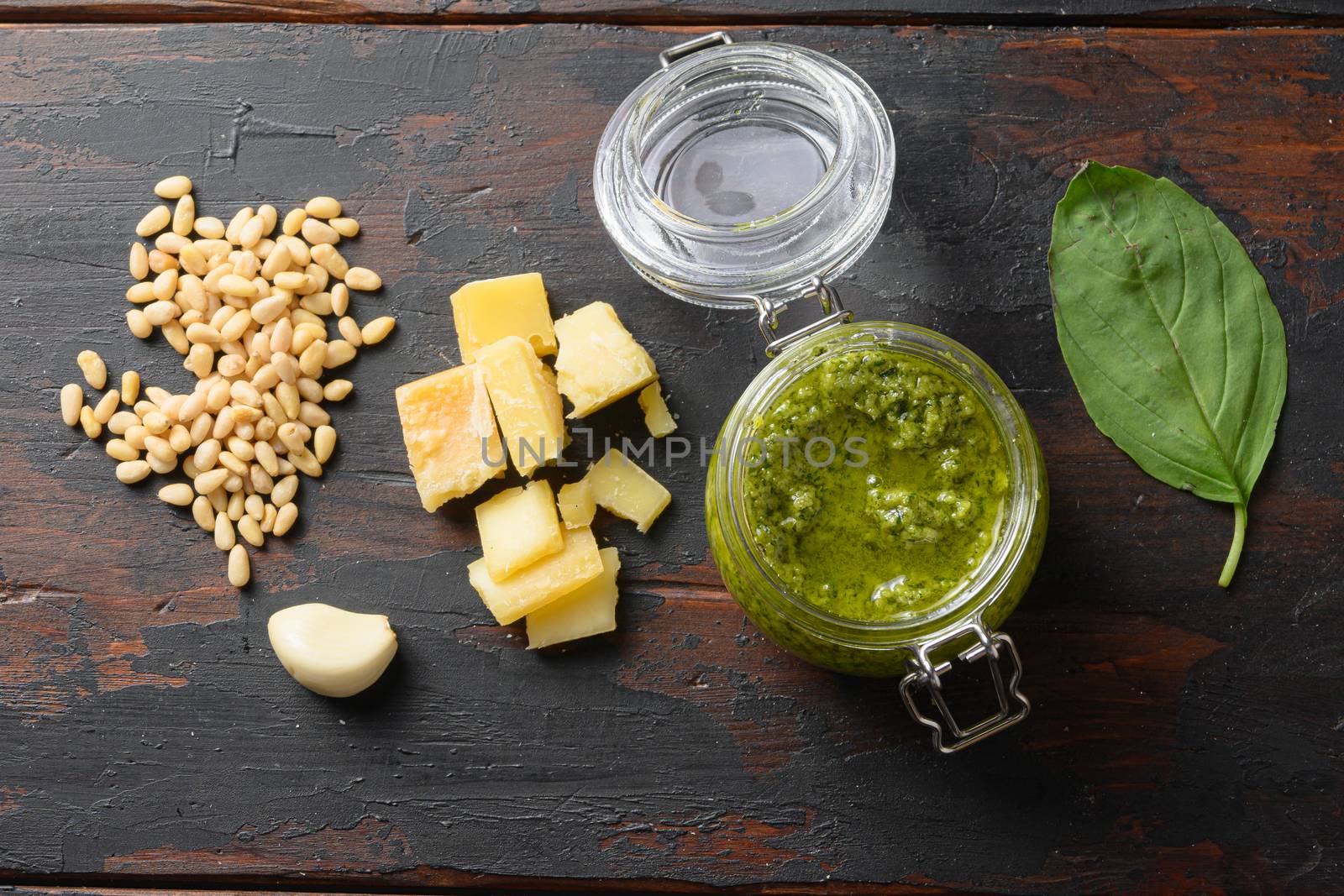 home made Pesto alla Genovese in glass jar with ingredients parmesan basil pine nuts . on dark wood table planks vintage top view by Ilianesolenyi