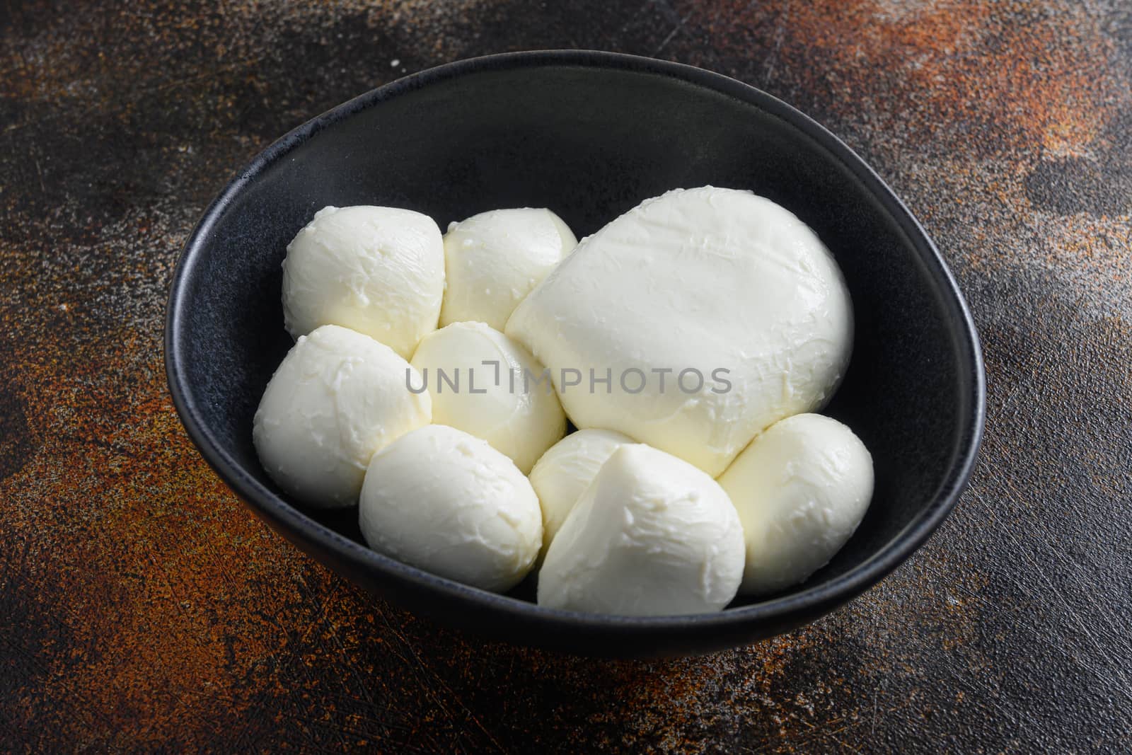 Mozzarella cheese balls in black bowl different size space for text over rustic surface dark metal style close up