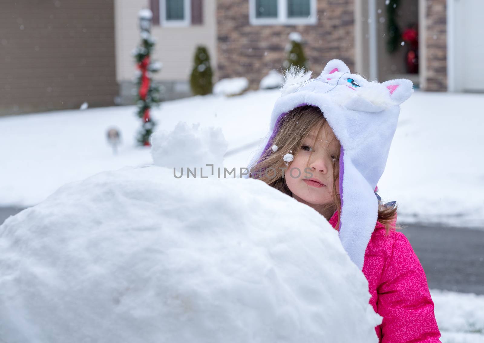 Young toddler girl playing in the snow and making a snowman