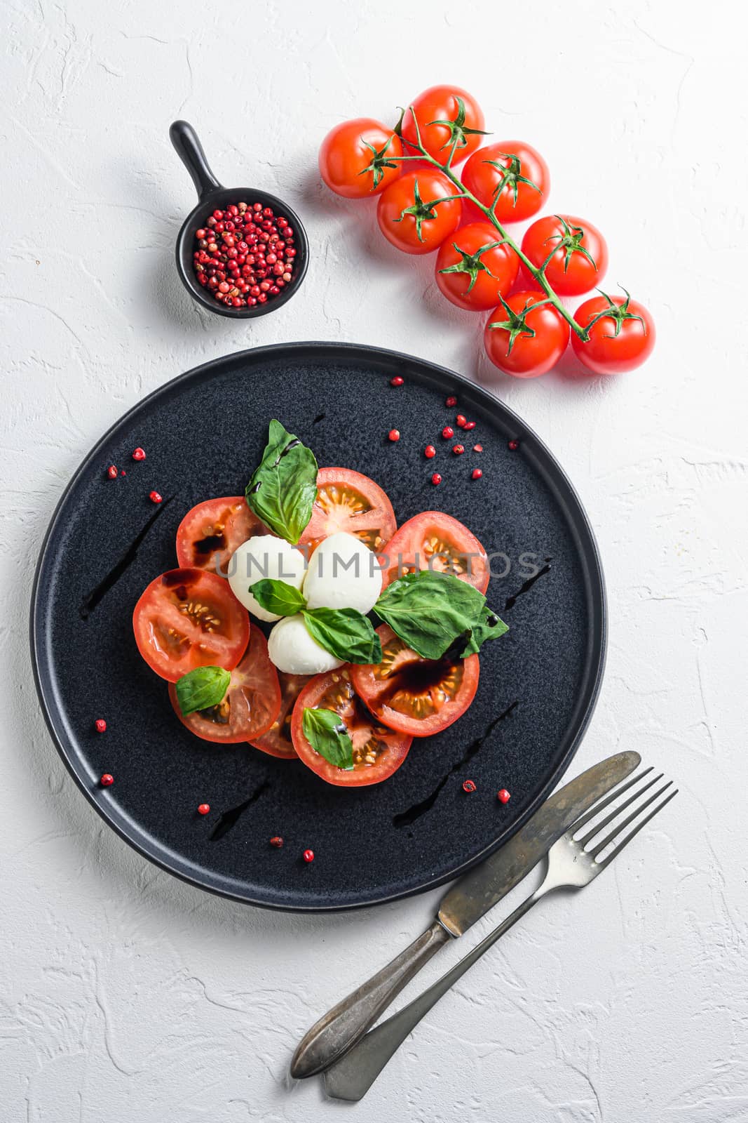 Caprese fresh italian salad with tomatoes, mozzarella, green basil on dark slate plate over white background top view selective focus vertical by Ilianesolenyi