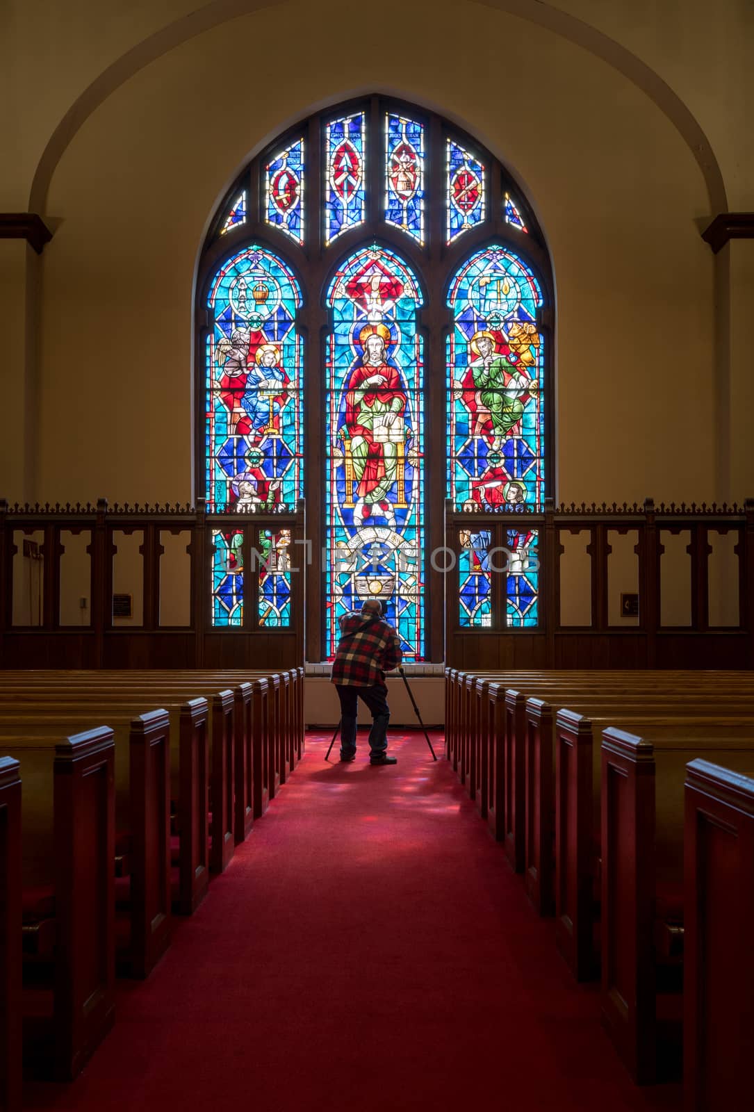 Photographer takes photo from the aisle between pews illuminated by light from stained glass window