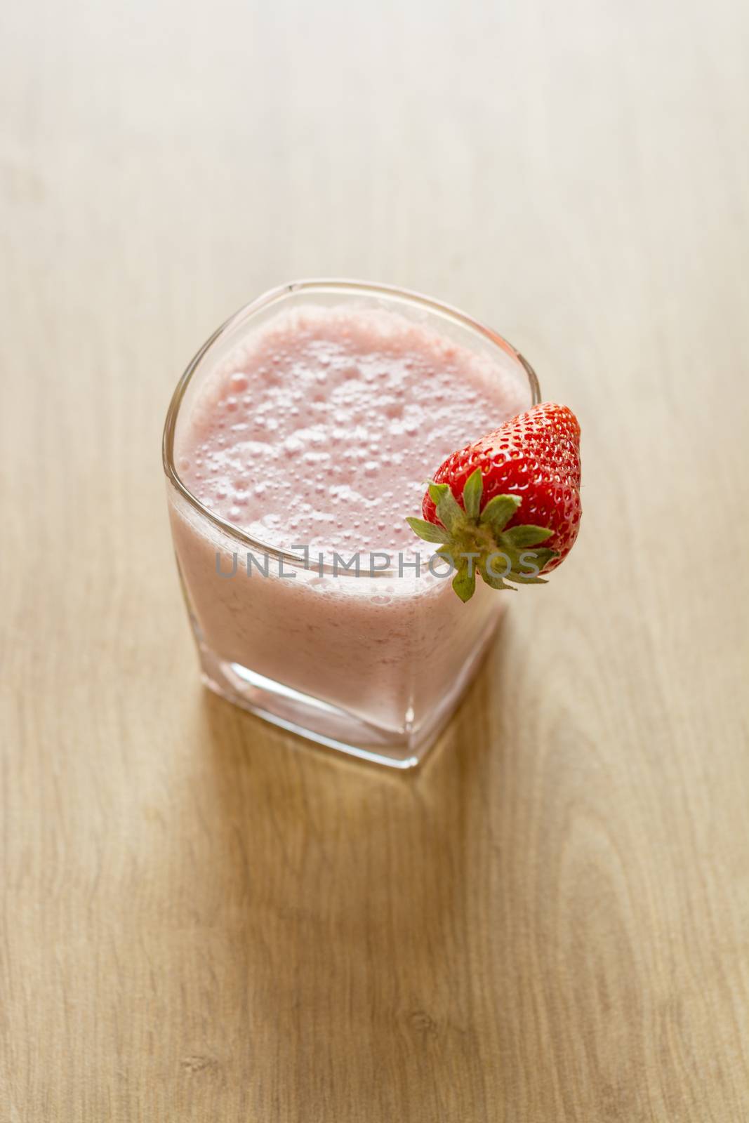 Fresh strawberry smoothie cold drink. Milkshake in glass on wooden table. Fruits for decoration