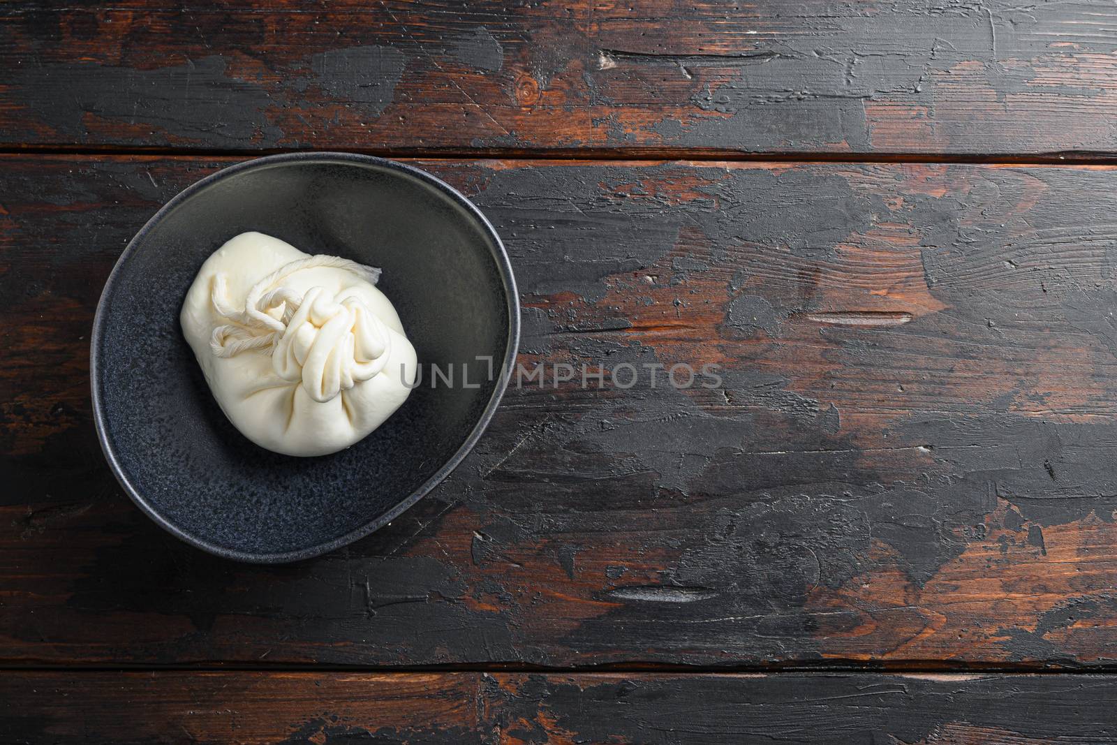 Creamy Italian Burrata Cheese in black plate over old wooden table< space for text horizontal.