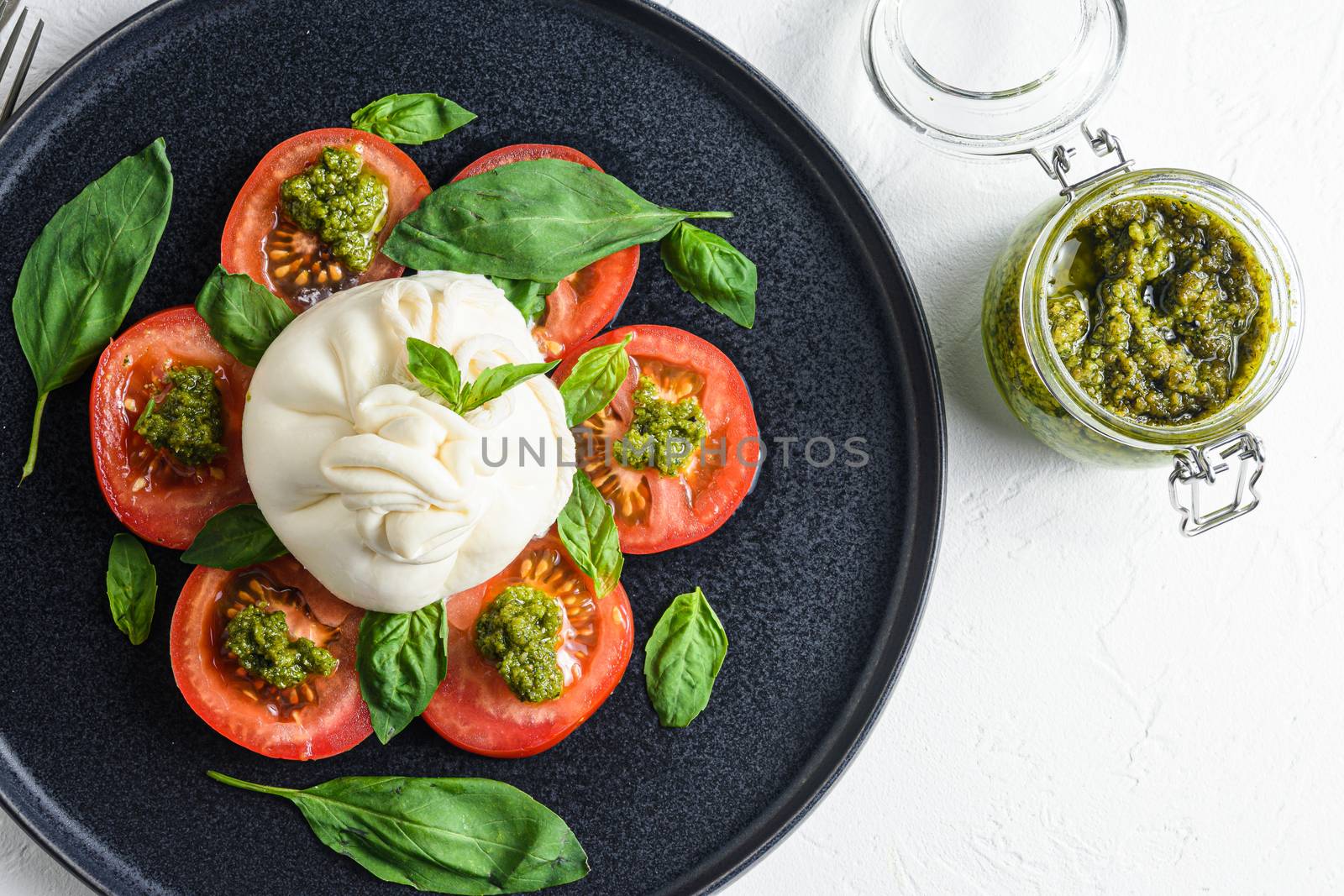 burrata Buffalo cheese served with fresh tomatoes and basil leaves pesto sauce on black plate white background flatlay by Ilianesolenyi