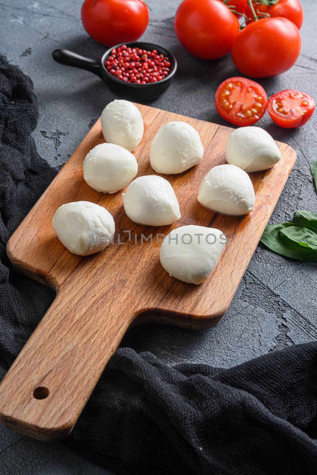 Buffalo Mozzarella cheese balls with fresh basil leaves and cherry tomatoes, the ingredients of the Italian Caprese salad, on a black cloth and grey concrete background close up vertical by Ilianesolenyi