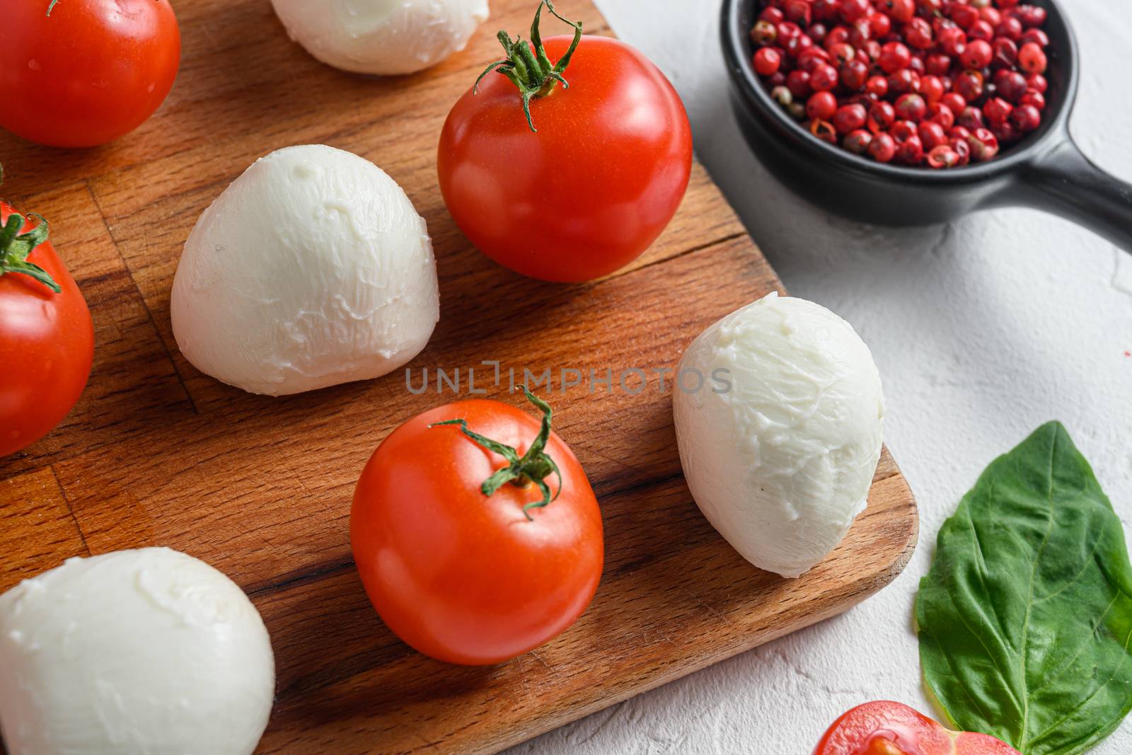 Mini balls of mozzarella cheese, on chop wood board ingredients for salad Caprese. over white background. close up selective focus.