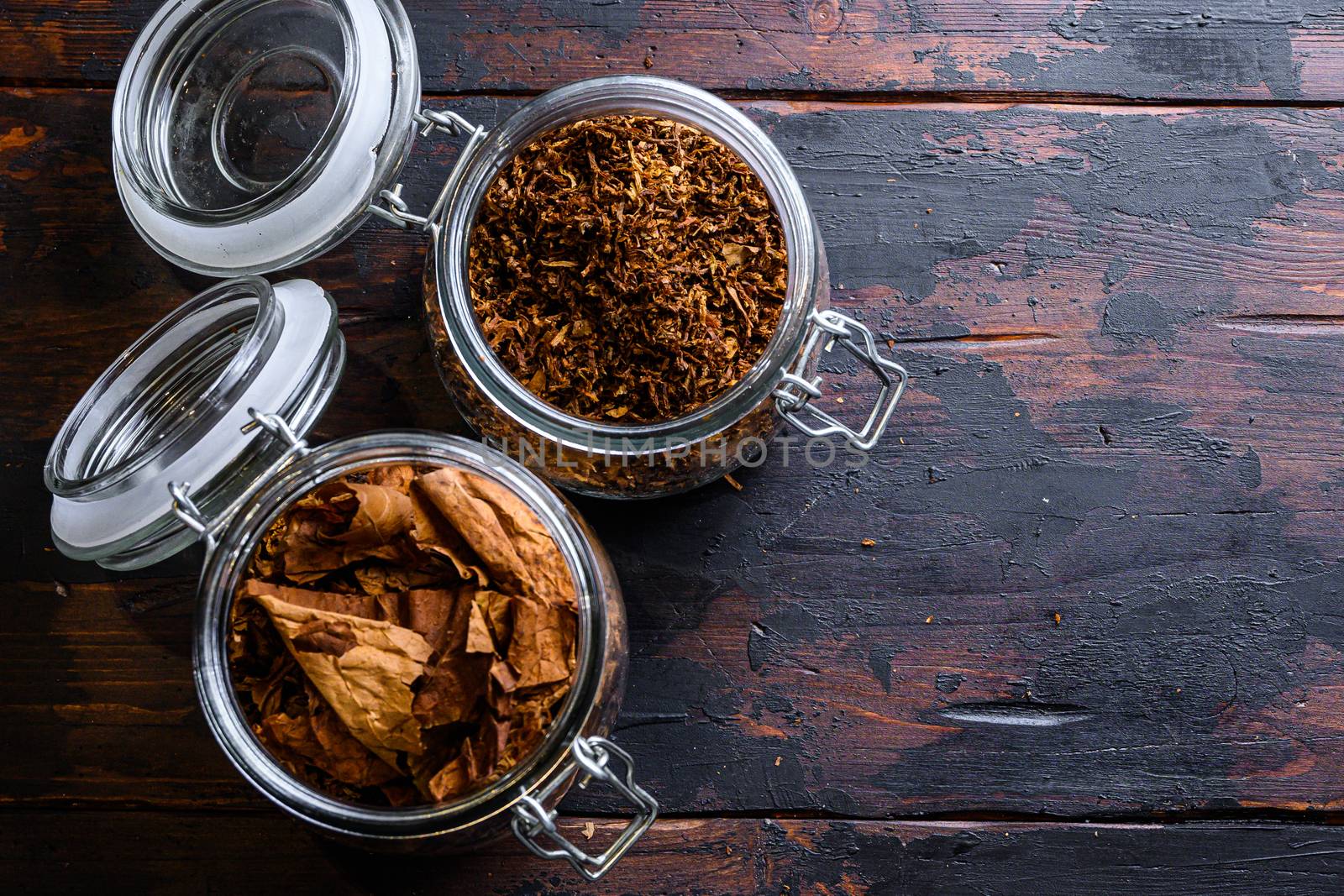 Cigar and pile of tobacco leaves of Dried tobacco in glass jars on rustic wood dark table top view space for text by Ilianesolenyi