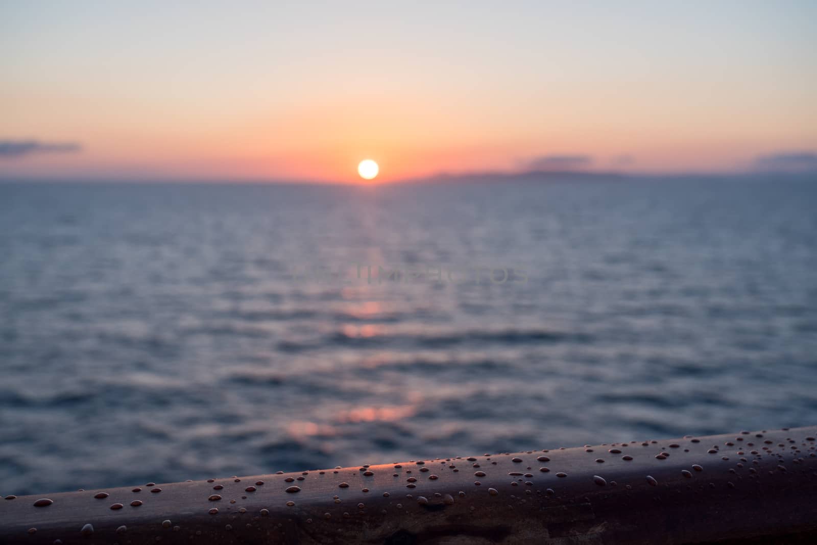 Water droplets on teak rail of small cruise liner sailing across the ocean as sun rises