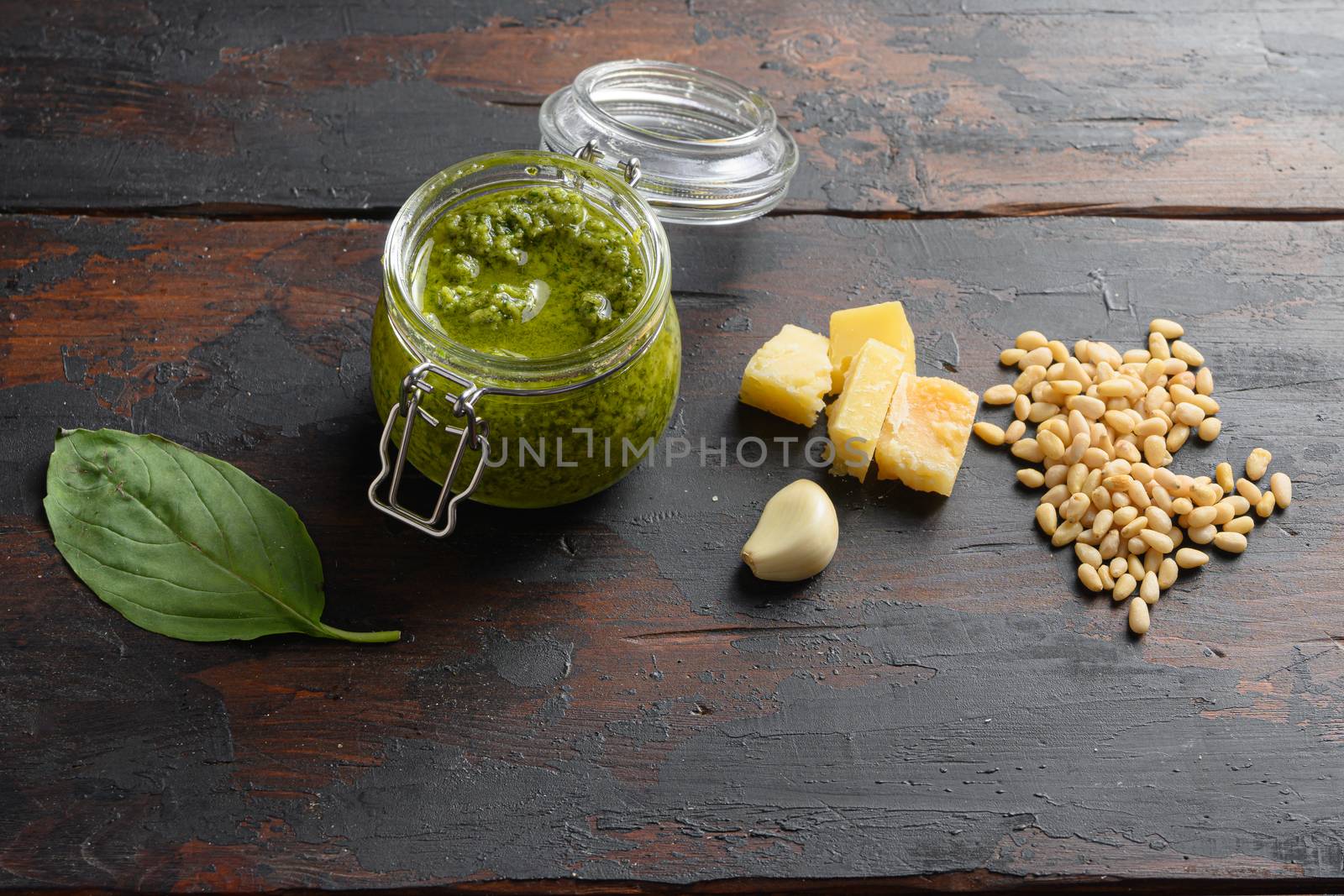 home made Pesto alla Genovese in glass jar with ingredients parmesan basil pine nuts. on dark wood table planks vintage side view by Ilianesolenyi