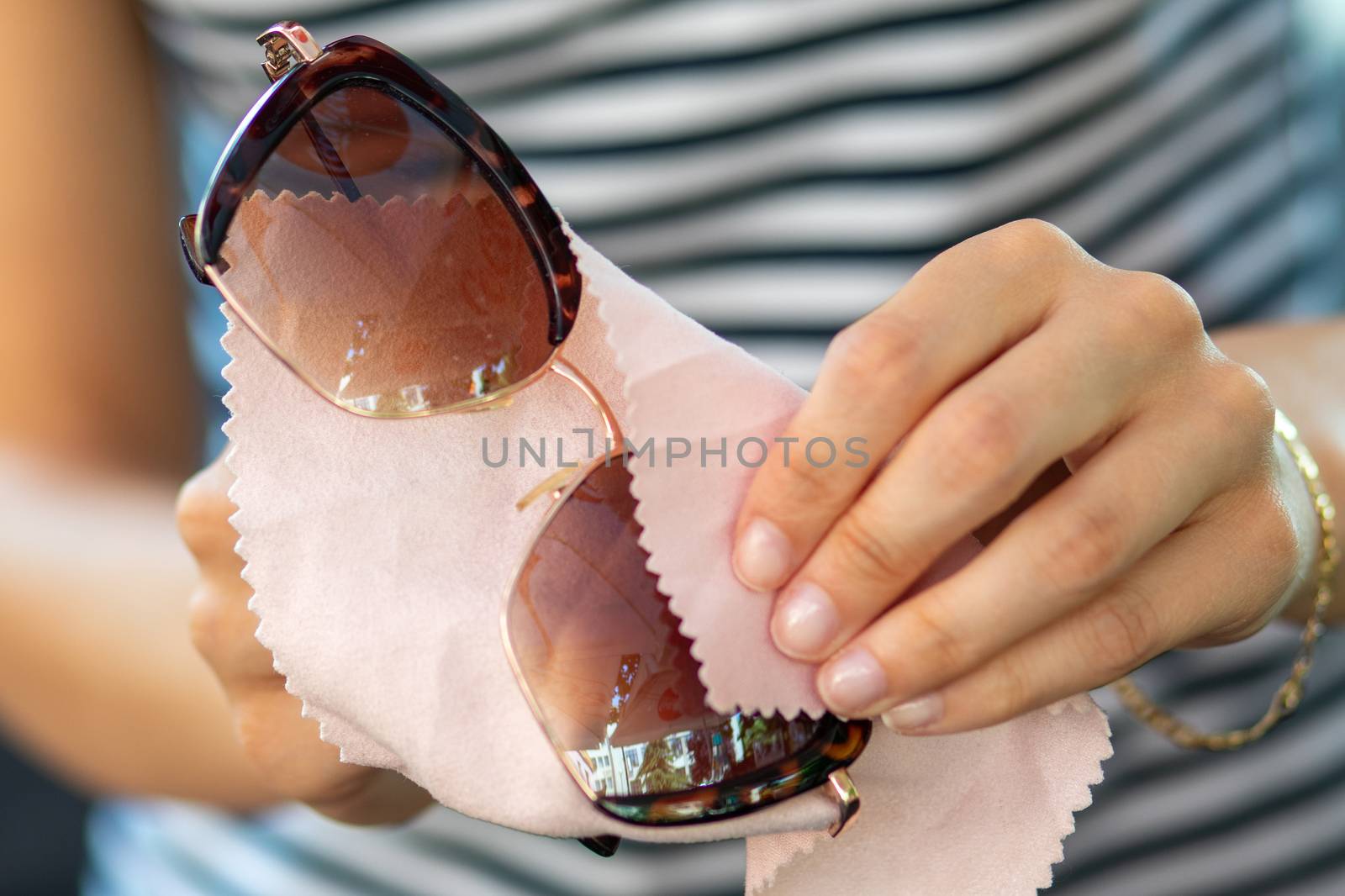 Woman hands cleaning her sunglasses glasses with micro fiber cloth wipe, wipping sunglasses