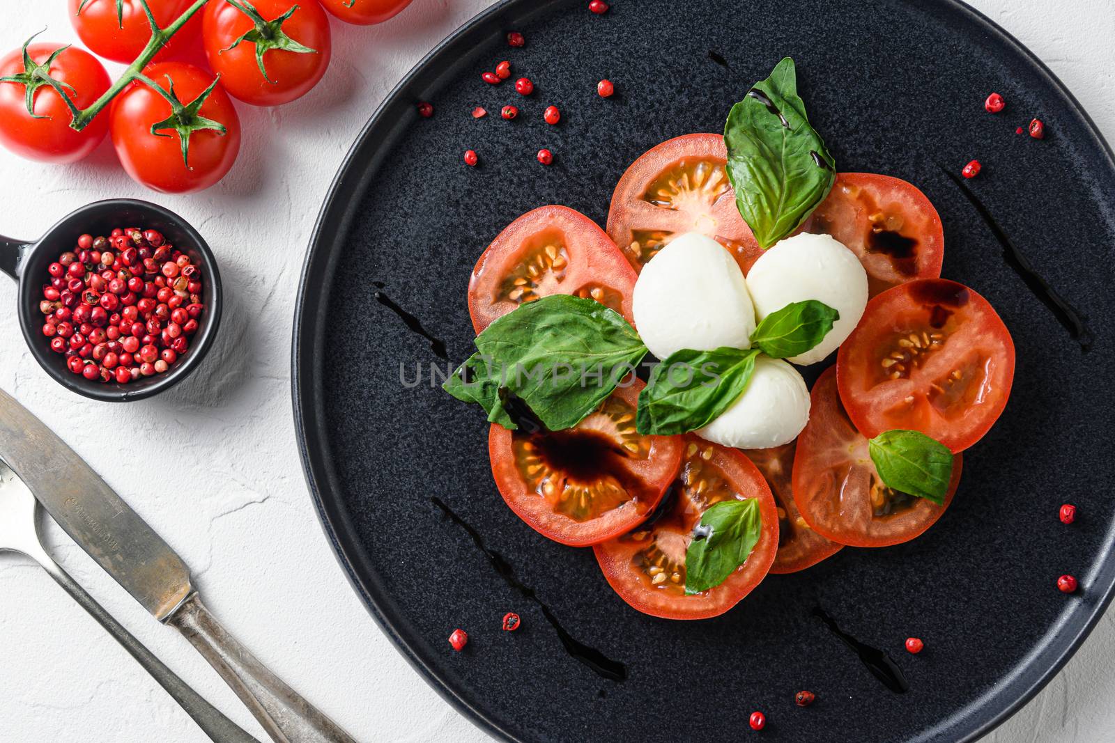 Caprese fresh italian salad with tomatoes, mozzarella, green basil on dark slate plate over white background top view by Ilianesolenyi