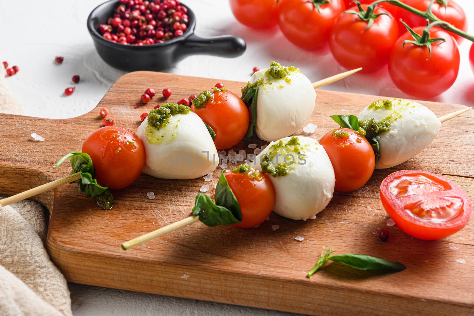 talian food - caprese salad - skewer with tomato, mozzarella and basil, pesto sauce, mediterranean diet concept on old chopping board and linen cloth close up.