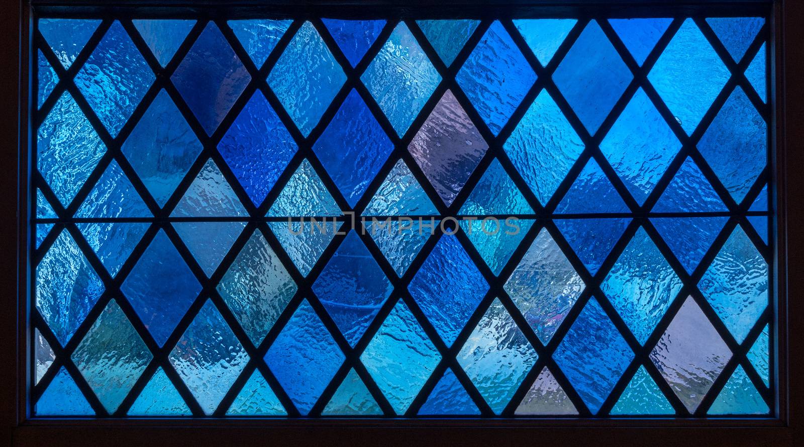 Detail of blue diamond shaped panes in colored light from stained glass window in catholic church