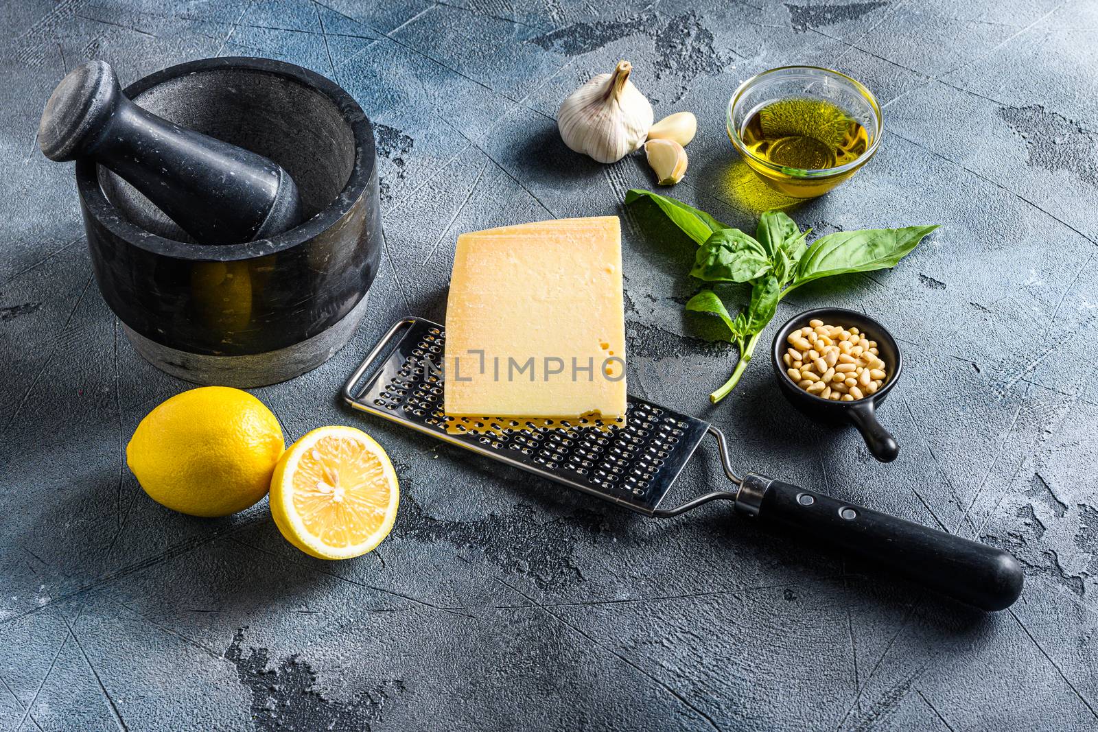 Green basil pesto italian recipe ingredients . Parmesan cheese, basil leaves, pine nuts, olive oil, garlic, salt, pepper and mortar. on gray concrete scratches stone background.