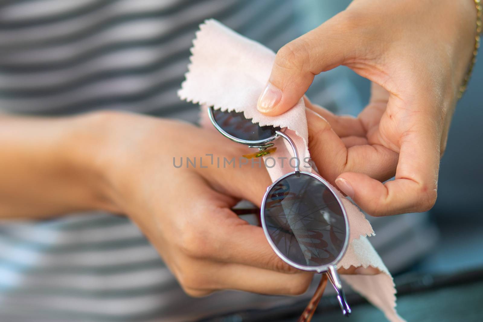 Woman hands cleaning her sun glasses with micro fiber cloth wipe, wiping sunglasses