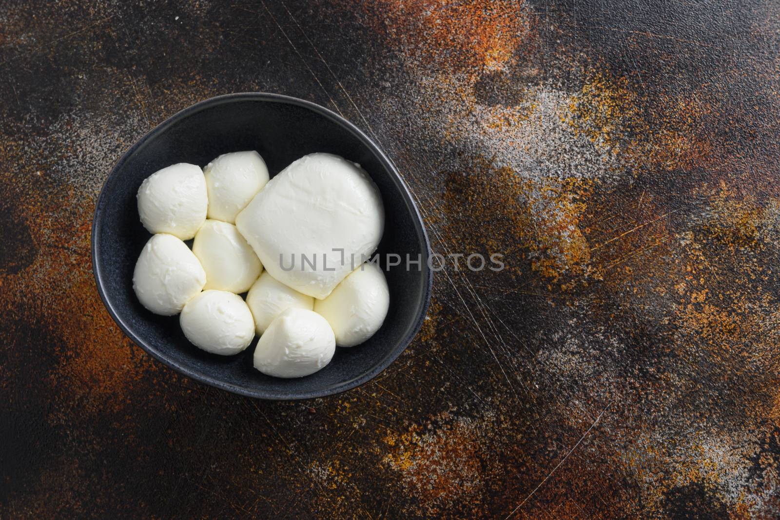 Mozzarella cheese balls in black bowl different size space for text over rustic surface dark metal style.