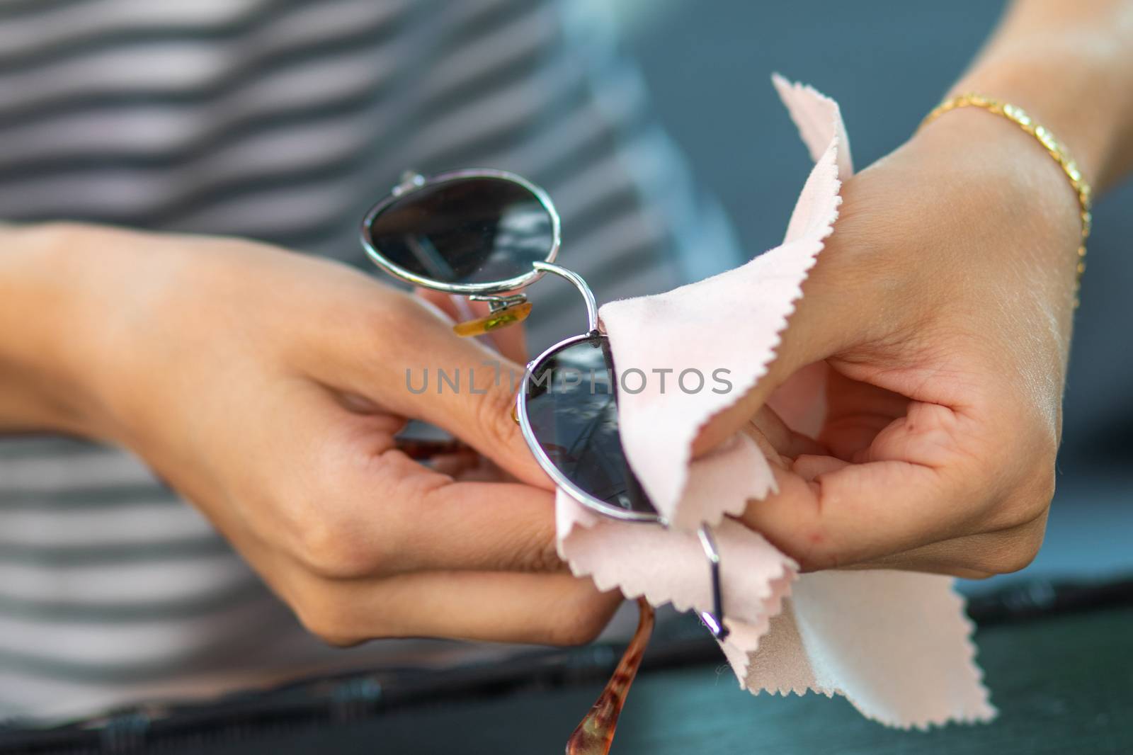 Woman with hands cleaning her sun glasses with micro fiber cloth wipe, wiping sunglasses