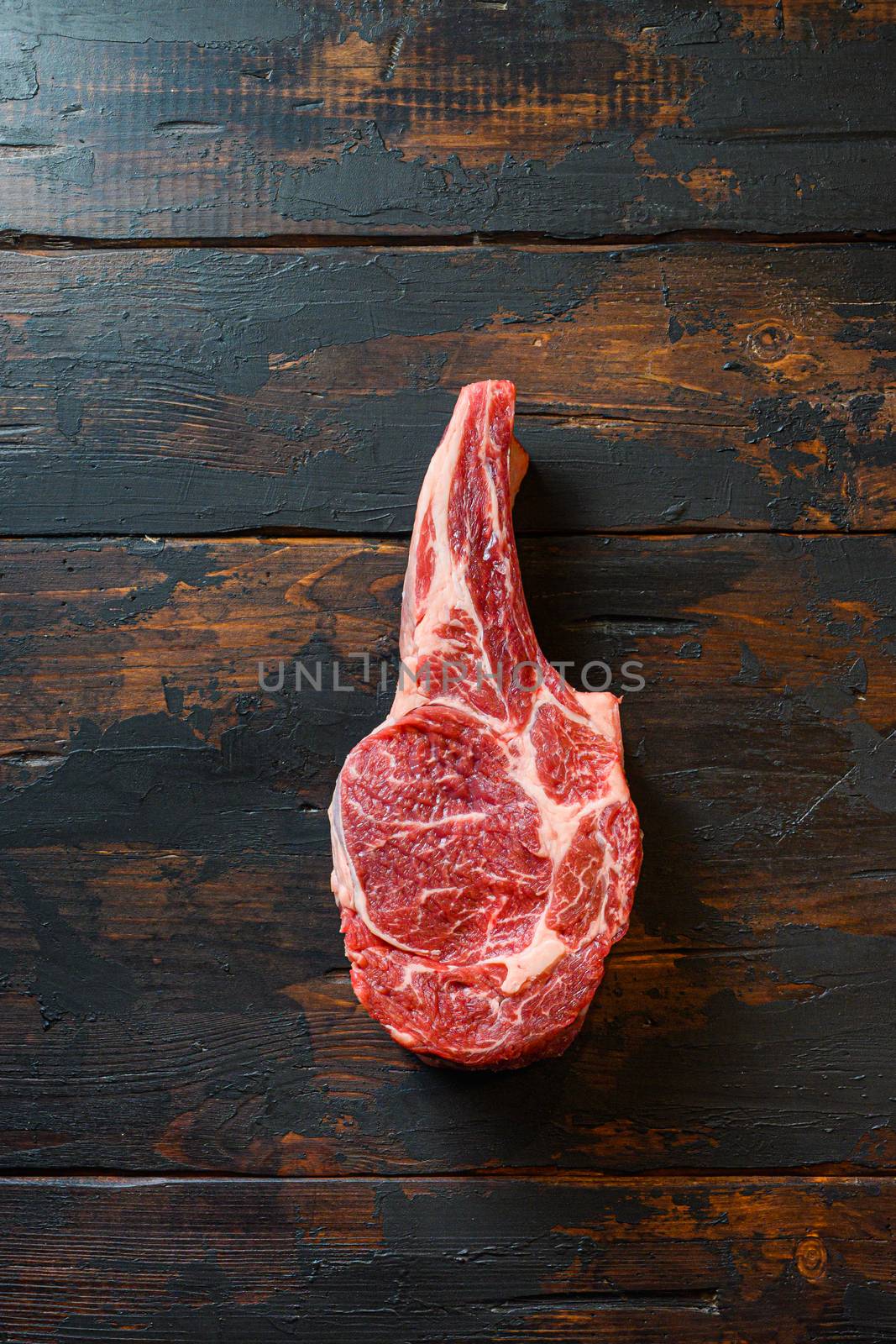 Raw uncooked black angus beef cowboy steak on bone on vintage dark wooden plank background. Top view, copy space.