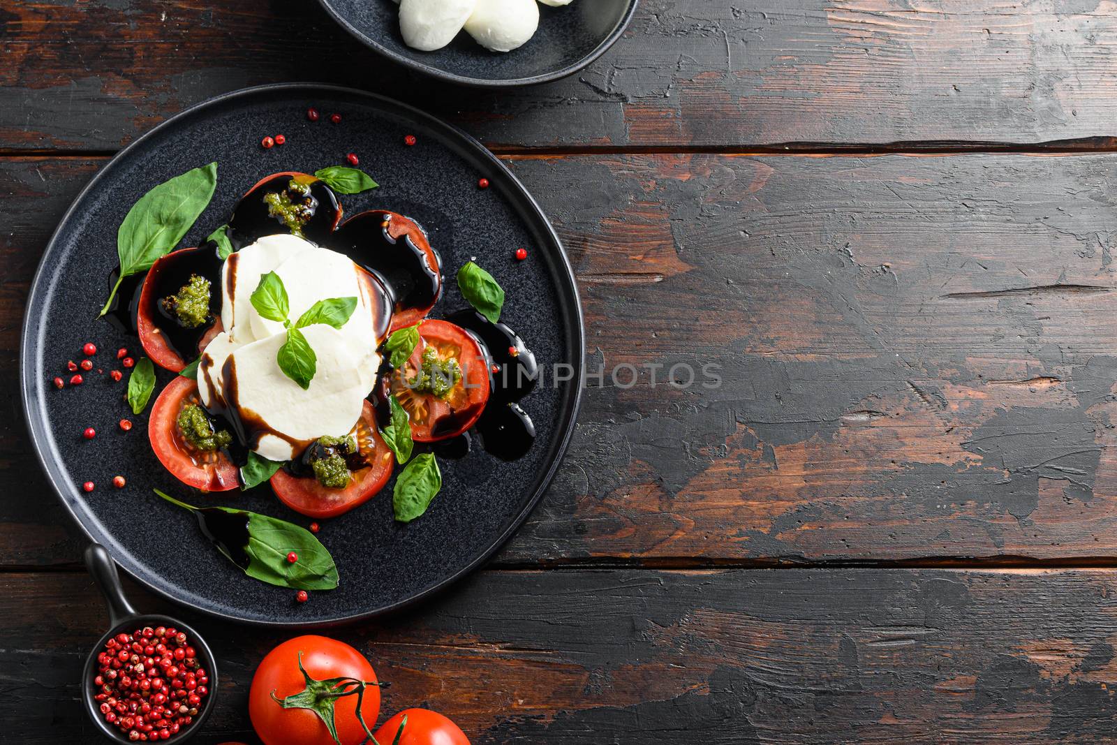 Italian food - caprese salad with sliced tomatoes, mozzarella cheese, basil, olive oil. Served on black plate over dark wood background. Top view. Rustic style. space for text layflat by Ilianesolenyi