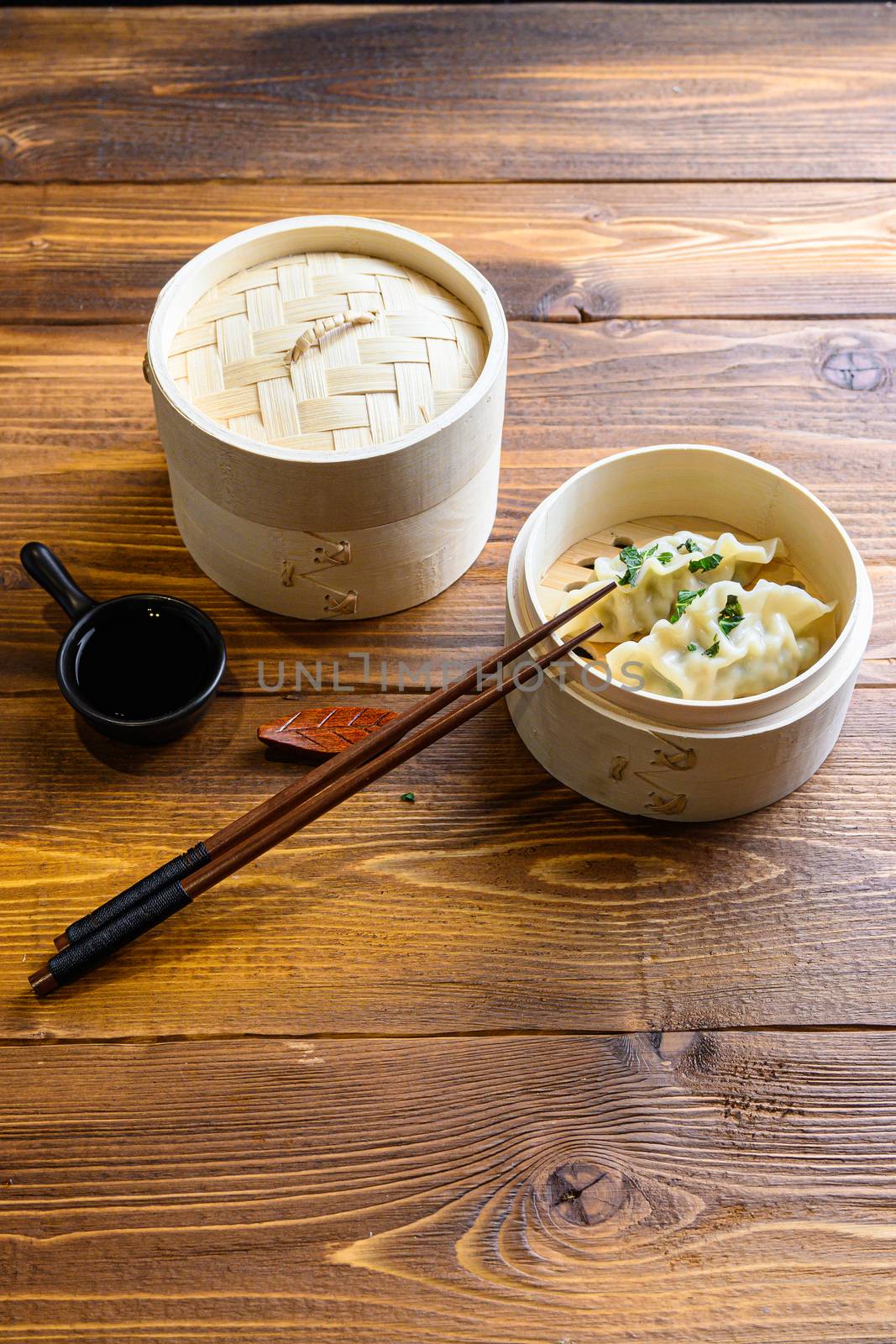 fresh boiled gyoza dumplings in wooden steamer with chopsticks soy sauce Chinese Traditional cuisine side view by Ilianesolenyi